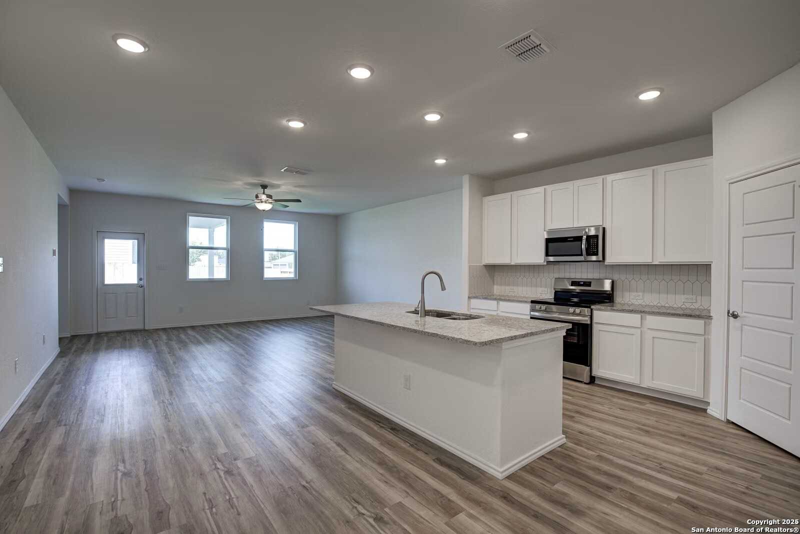 Modern open-concept kitchen with white cabinets, stainless appliances, large island, and hardwood floors in Davidson Homes The Douglas B, Seguin, Texas