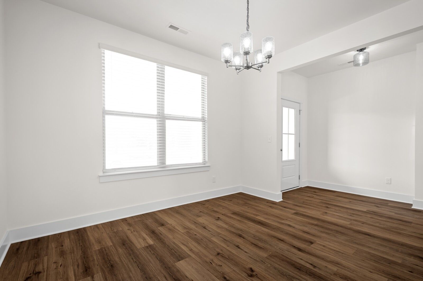 Bright dining area with modern chandelier and wood-look flooring in The Ash A floor plan at Woods Crossing, Gallatin.