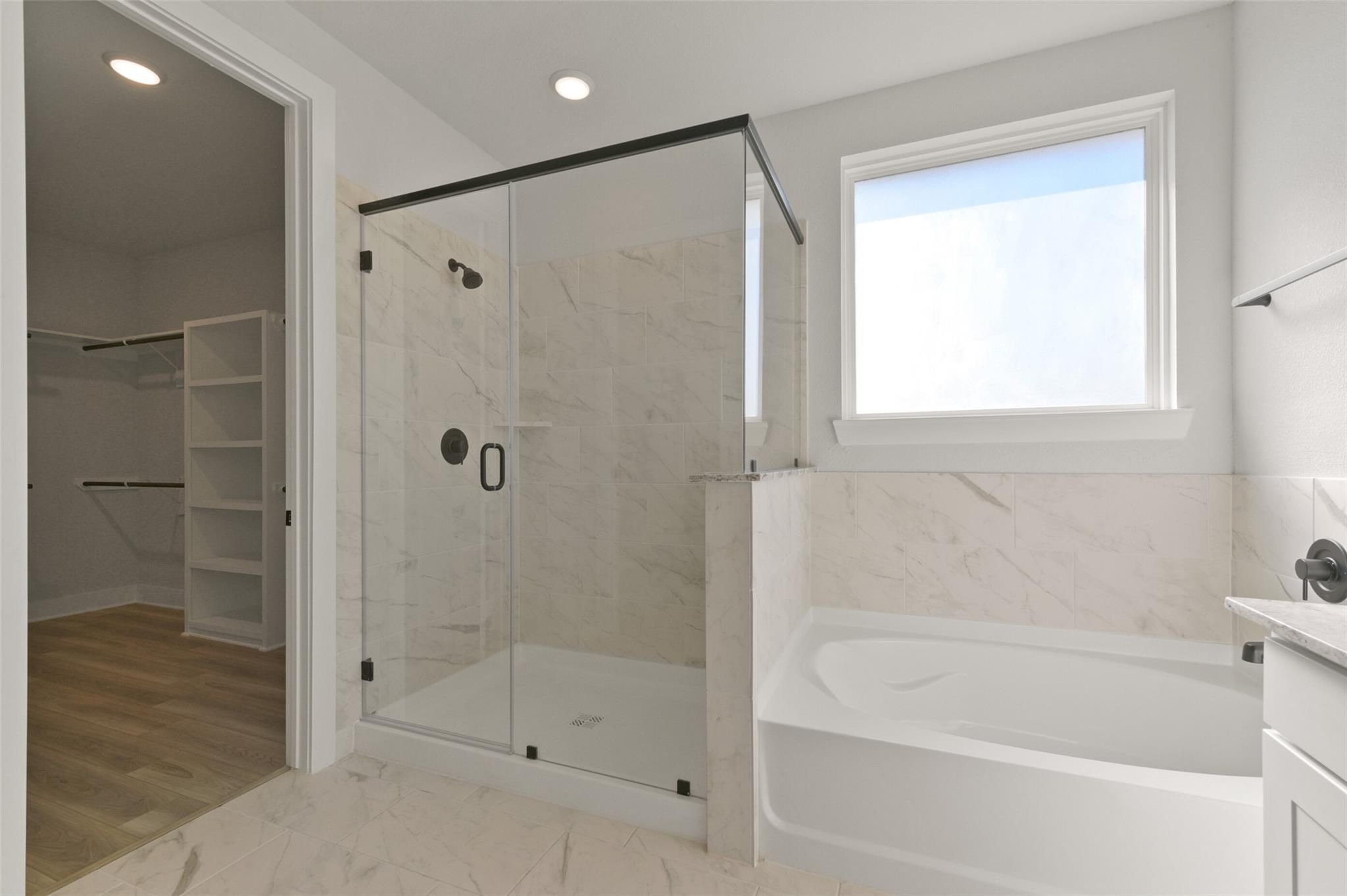 Modern master bathroom with frameless glass shower, marble tiles, freestanding tub, and walk-in closet in Davidson Homes The Edward C, Lago Mar, Texas