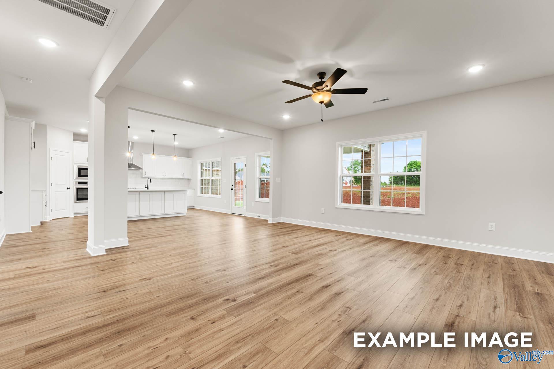 Open-concept kitchen and living room with white cabinets, hardwood floors, ceiling fan, and French doors in Davidson Homes Madison B, Toney Alabama