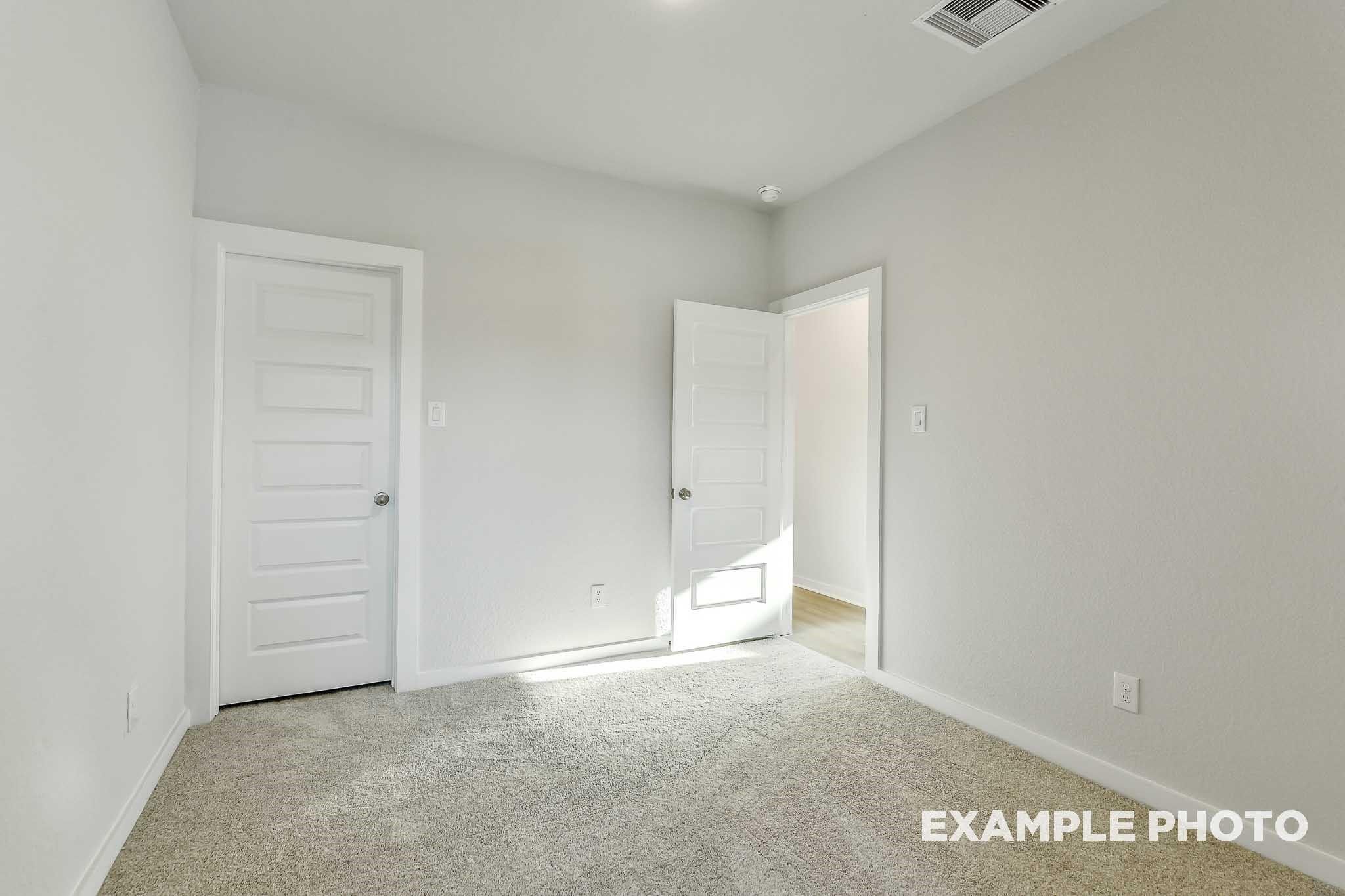 Empty secondary bedroom with neutral walls, beige carpet, and open doorway in Davidson Homes The Colorado G, Conroe, Texas