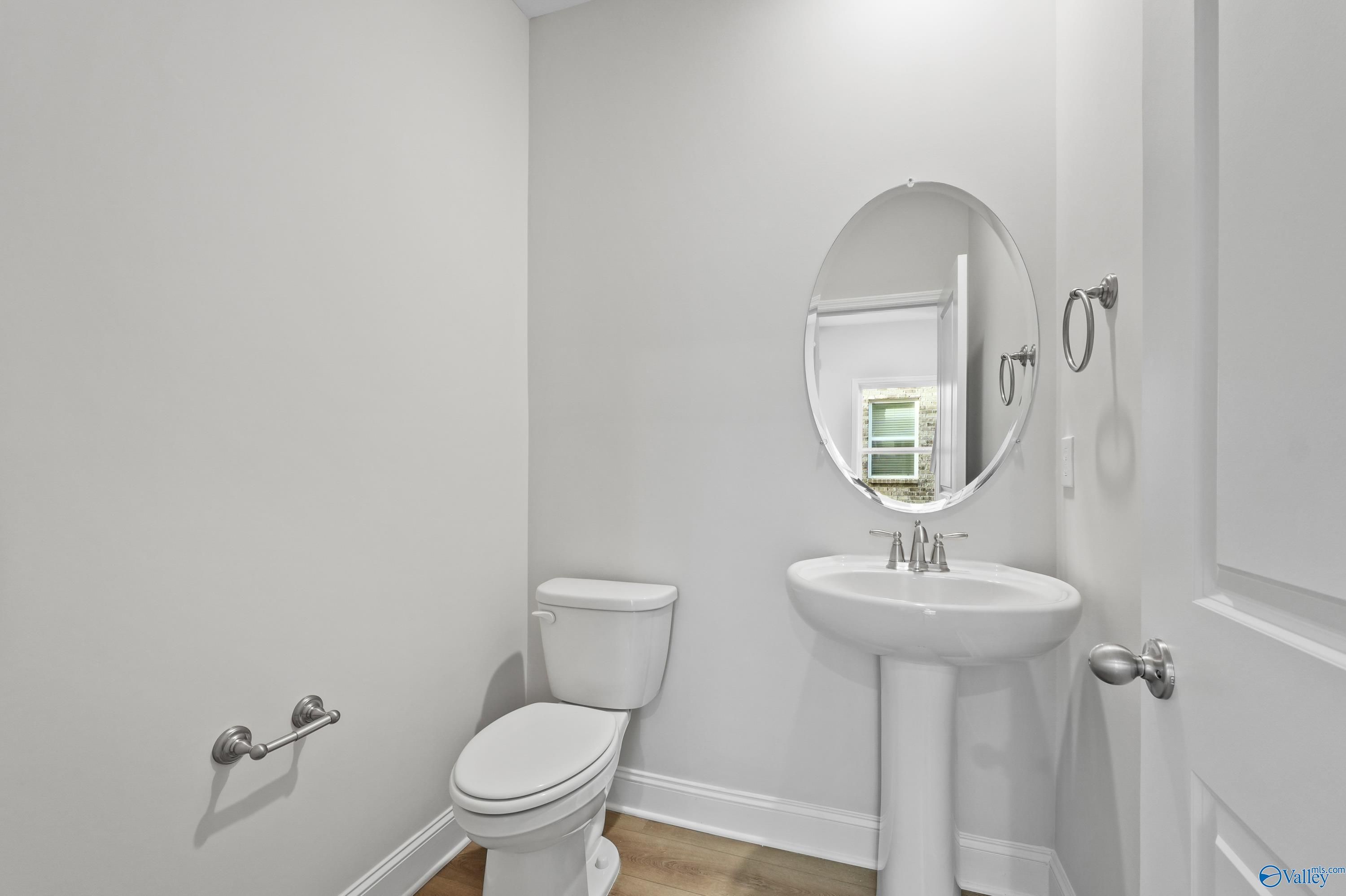 Bright white powder room featuring pedestal sink, round mirror, and toilet in Davidson Homes The Camden, Huntsville, Alabama