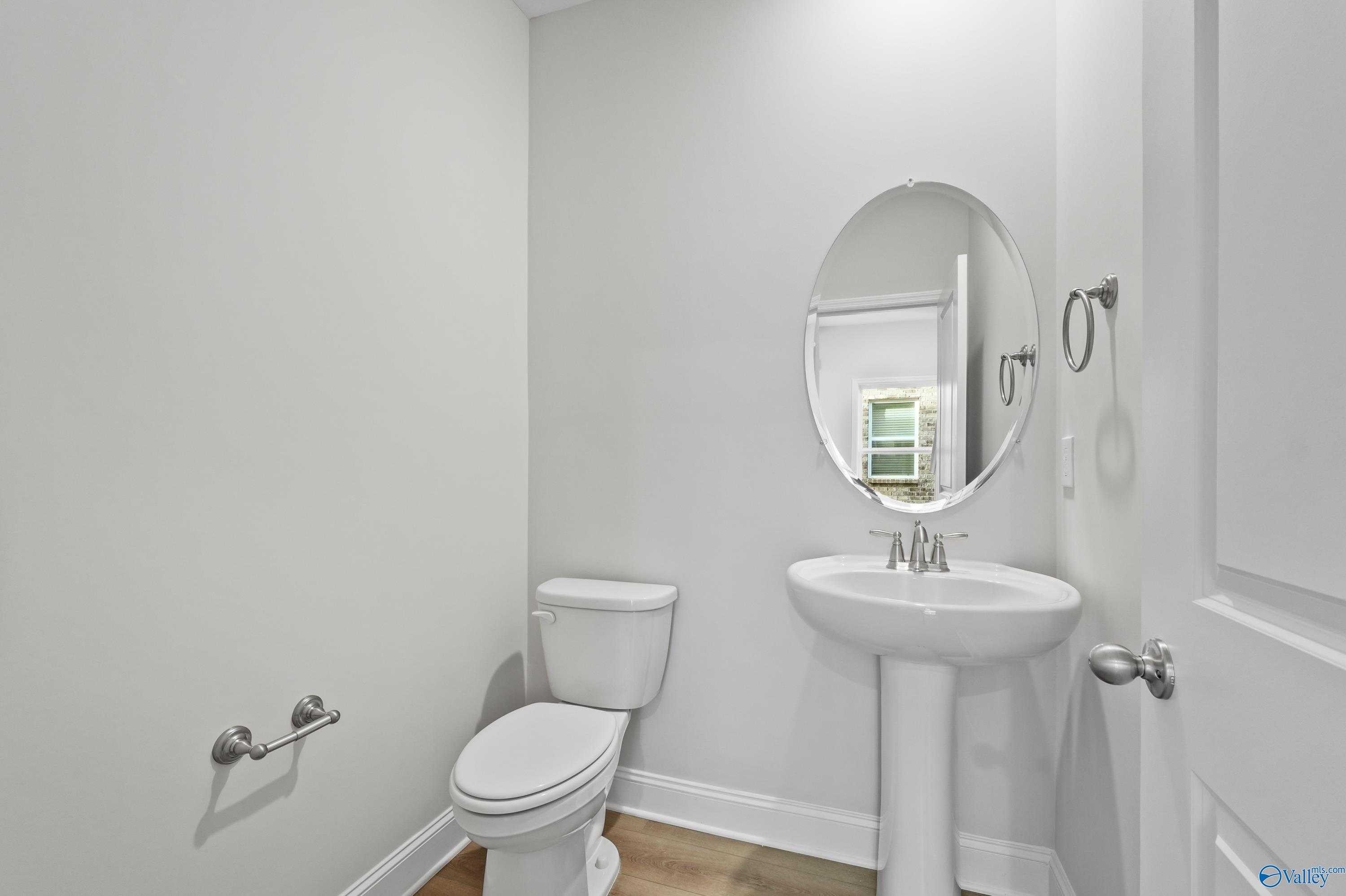 Bright white powder room featuring pedestal sink, round mirror, and toilet in Davidson Homes The Camden, Huntsville, Alabama