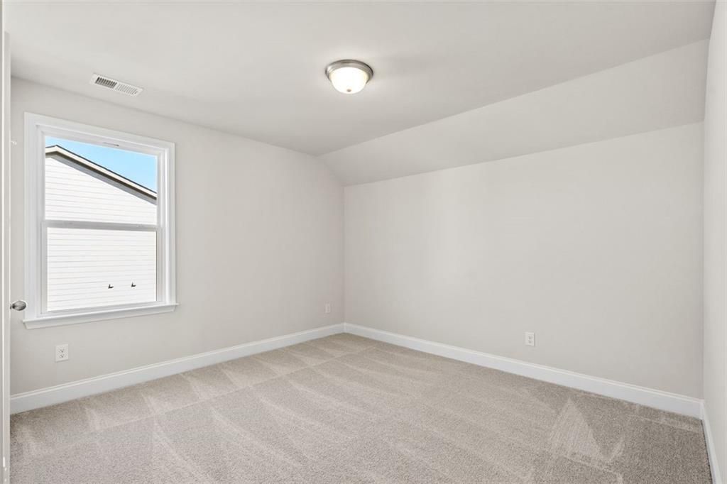 Bright secondary bedroom with white walls, beige carpet, and window overlooking neighborhood in Davidson Homes The Ash C, Hoschton