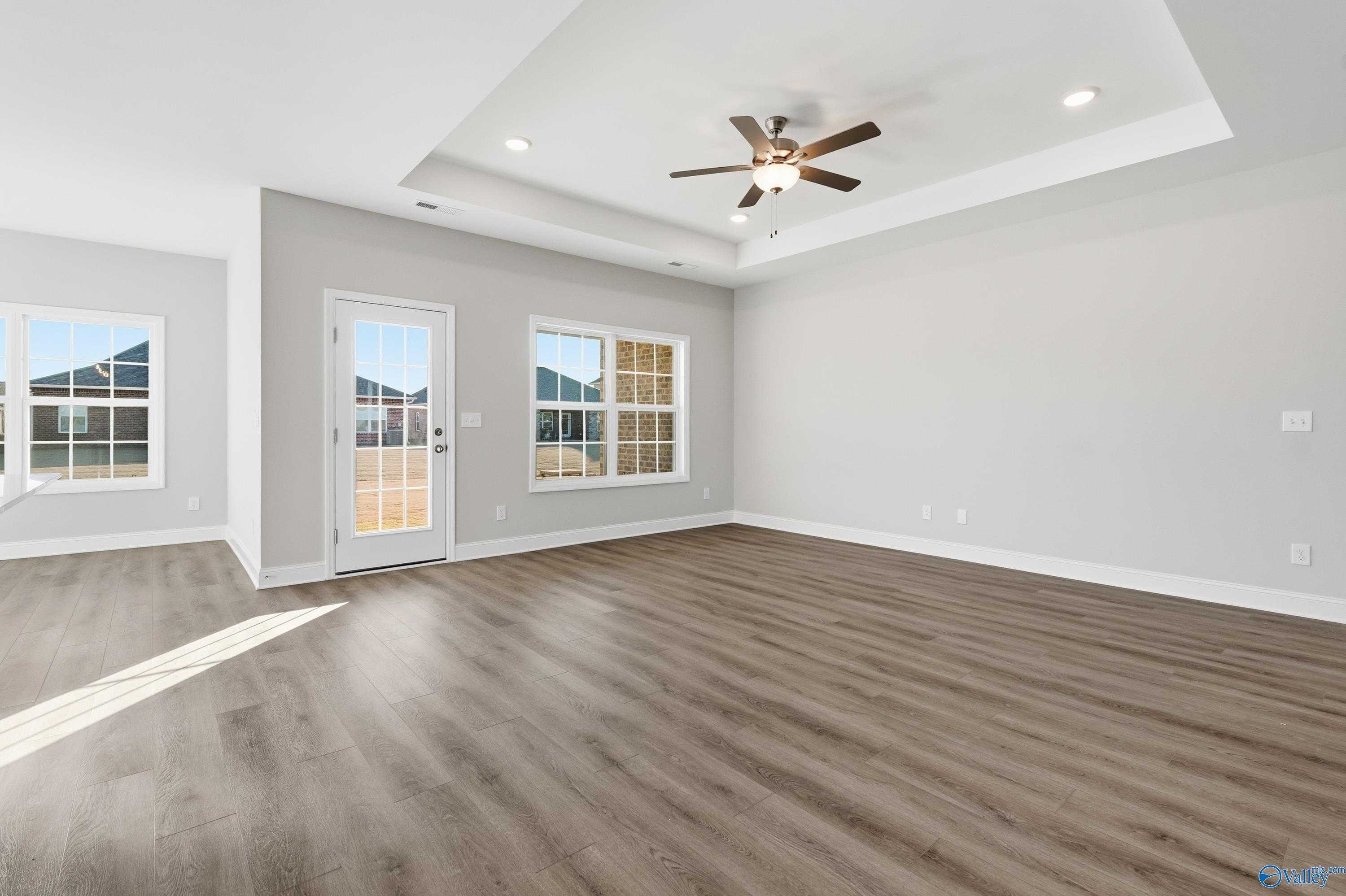 Spacious living room with ceiling fan, large windows, sliding door, and hardwood floors in The Montgomery B, Toney, Alabama