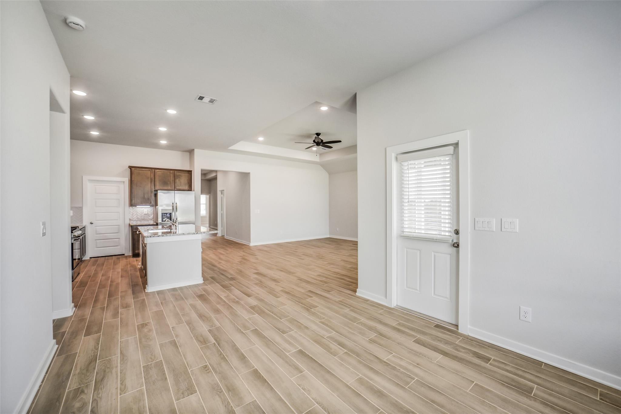 Open-concept kitchen with white island, wood cabinets, and stainless appliances in Davidson Homes The Acadia C, Magnolia Texas