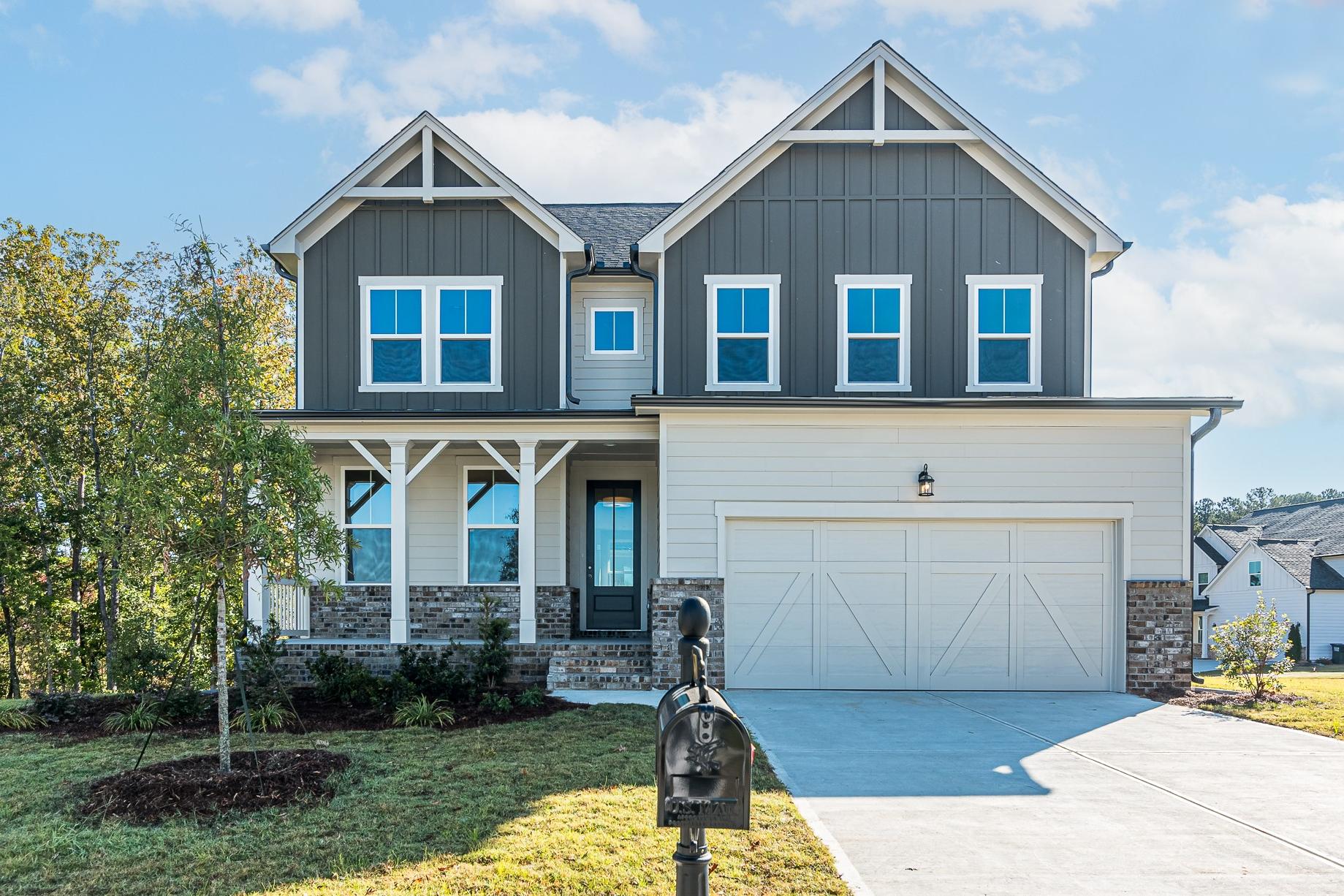 Modern two-story The Willow B home elevation at Wehunt Meadows with gray siding, stone accents, covered porch, and two-car garage in Hoschton, GA