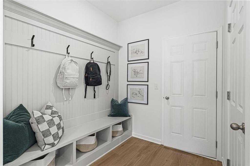 Functional mudroom with wainscoted walls, hanging backpacks, built-in bench with pillows, and storage baskets in Davidson Homes The Hickory B, Hoschton, GA