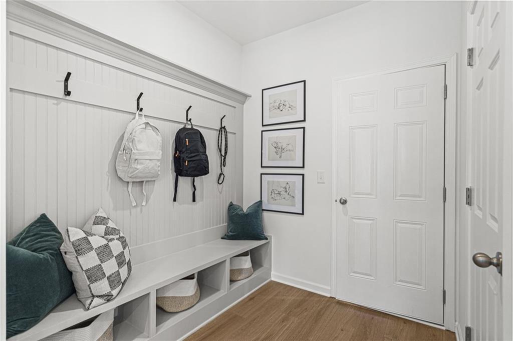 Functional mudroom with wainscoted walls, hanging backpacks, built-in bench with pillows, and storage baskets in Davidson Homes The Hickory B, Hoschton, GA