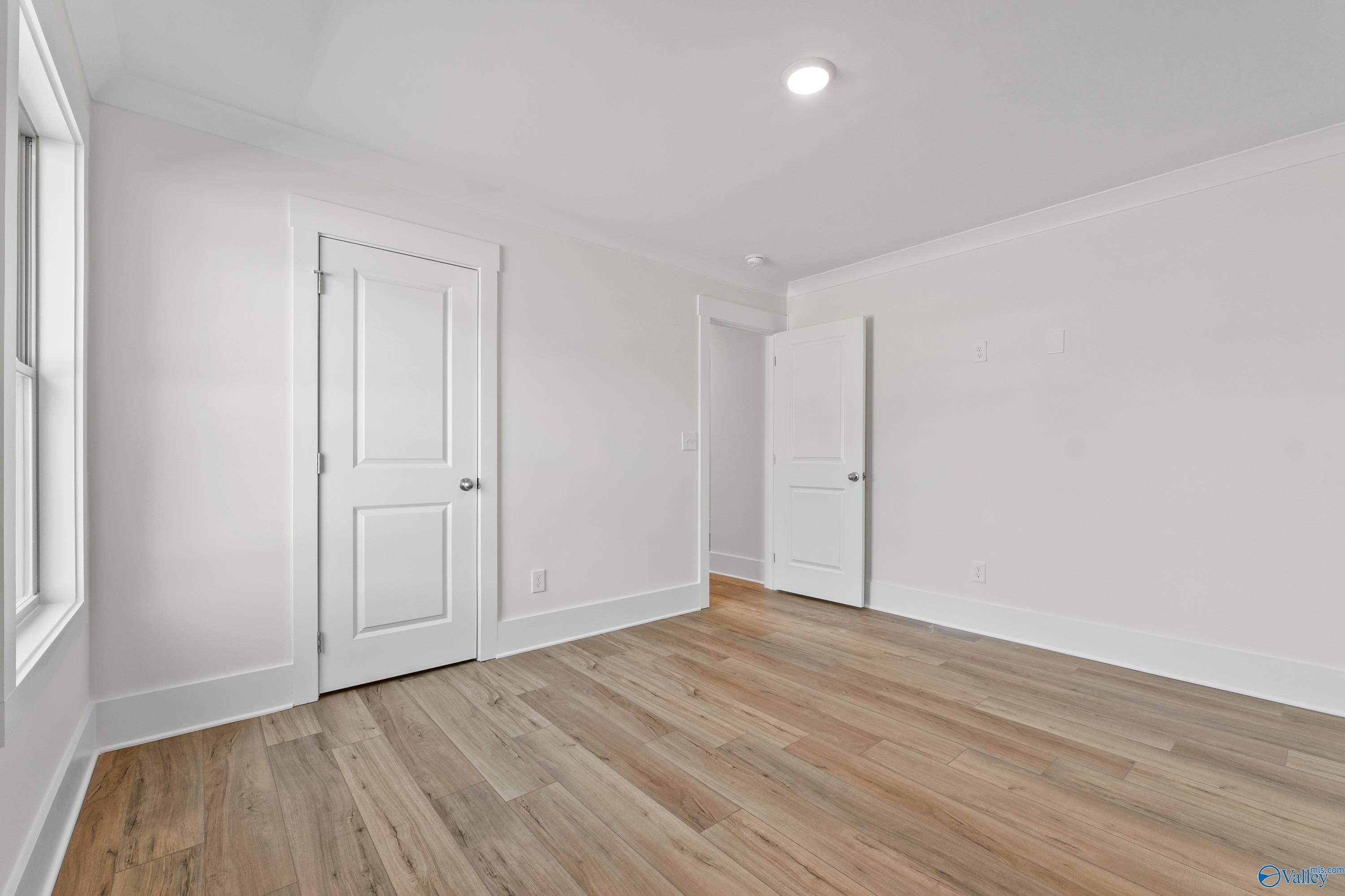Bright bedroom with oak hardwood floors, white walls, and double doors in Davidson Homes The Daphne C, Arab, Alabama