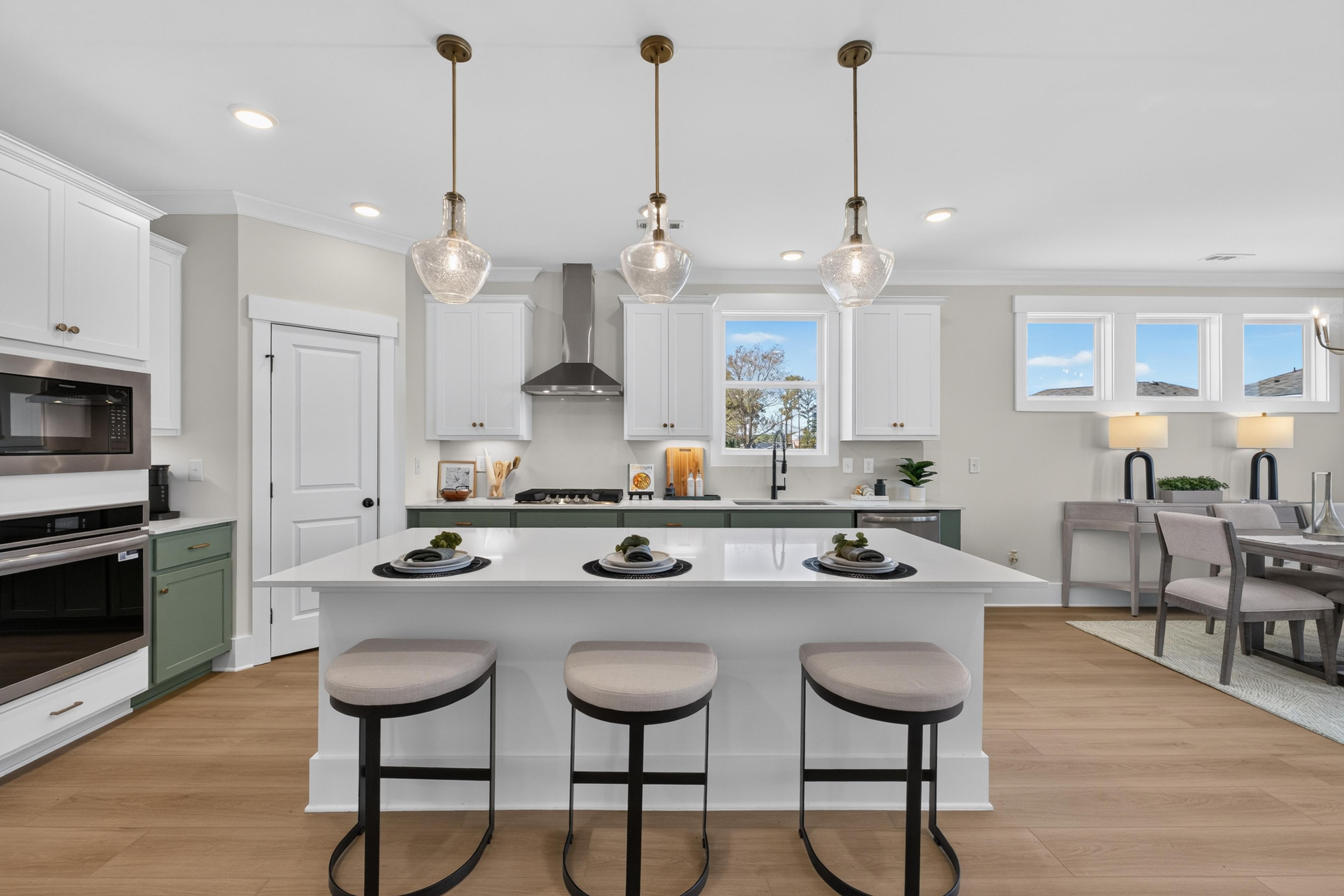 Kitchen island with white and sage green cabinets, pendant lights, and barstools at Evergreen Mill in Madison, Alabama by Davidson Homes