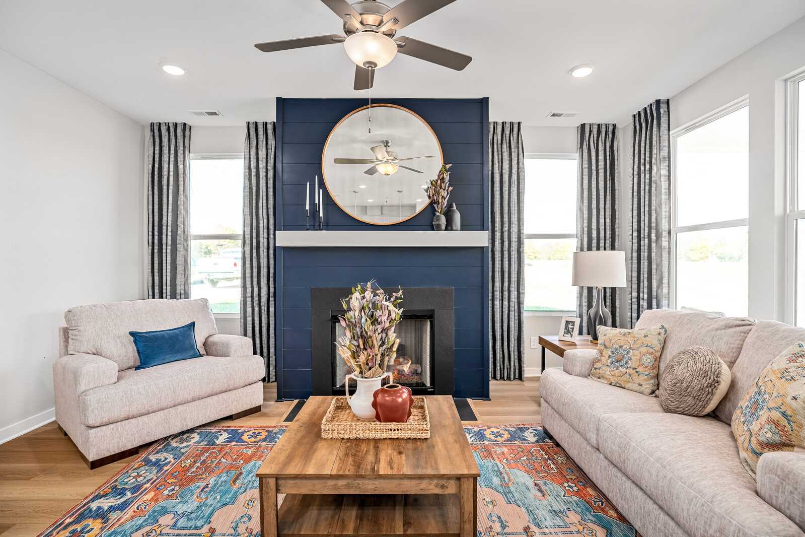 Open-concept living room at Sage Farms in White House TN with navy accent wall, round mirror over fireplace, plush beige seating, and hardwood floors