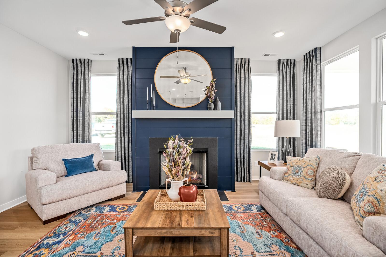Open-concept living room at Sage Farms in White House TN with navy accent wall, round mirror over fireplace, plush beige seating, and hardwood floors