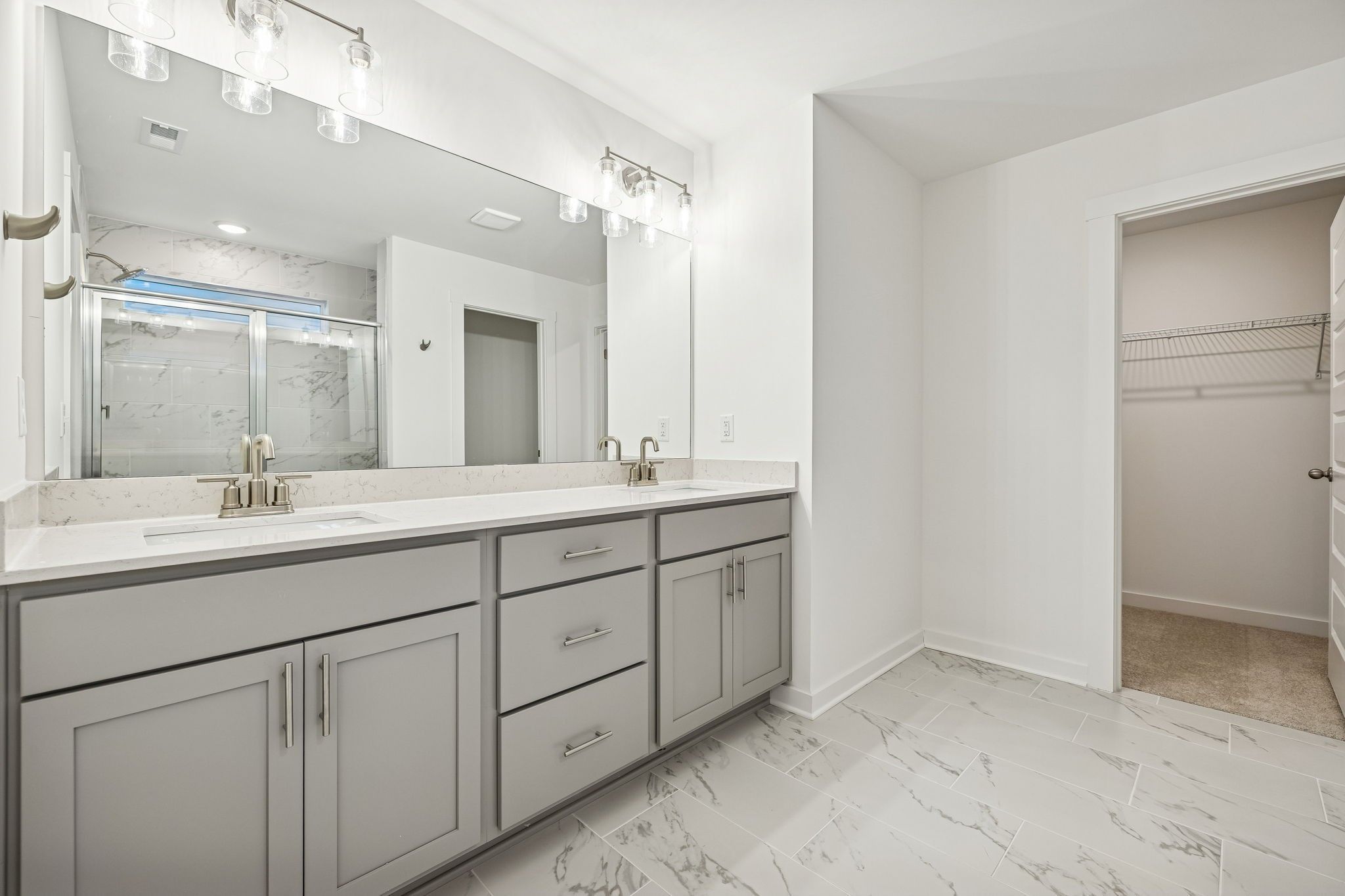 Modern master bathroom with double gray vanity, quartz counters, glass marble shower, and walk-in closet in Davidson Homes The Willow