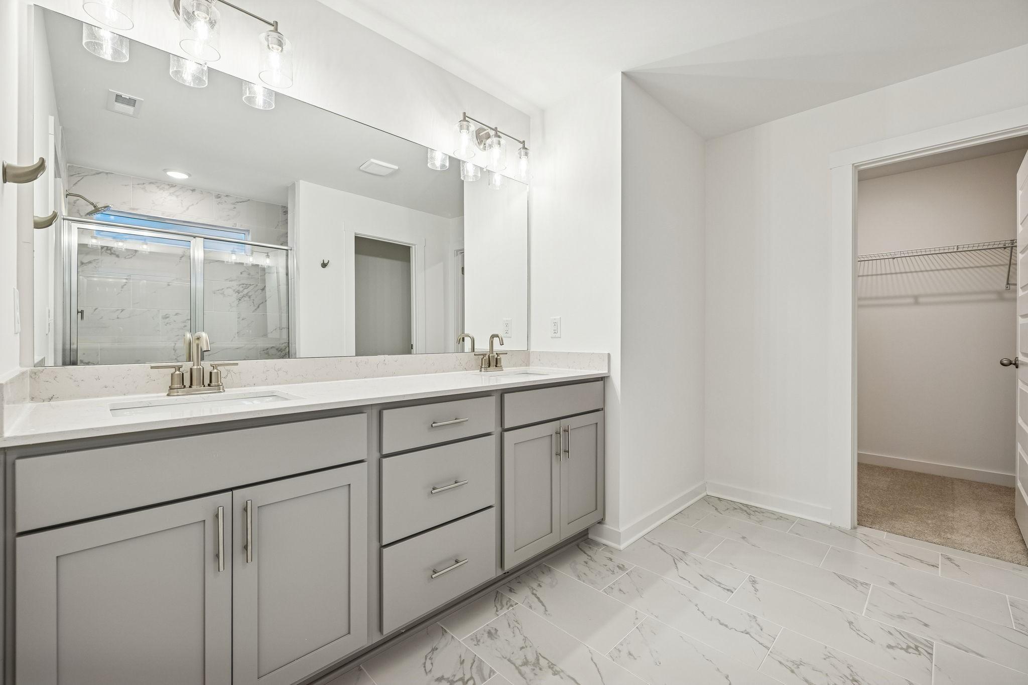 Modern master bathroom with double gray vanity, quartz counters, glass marble shower, and walk-in closet in Davidson Homes The Willow
