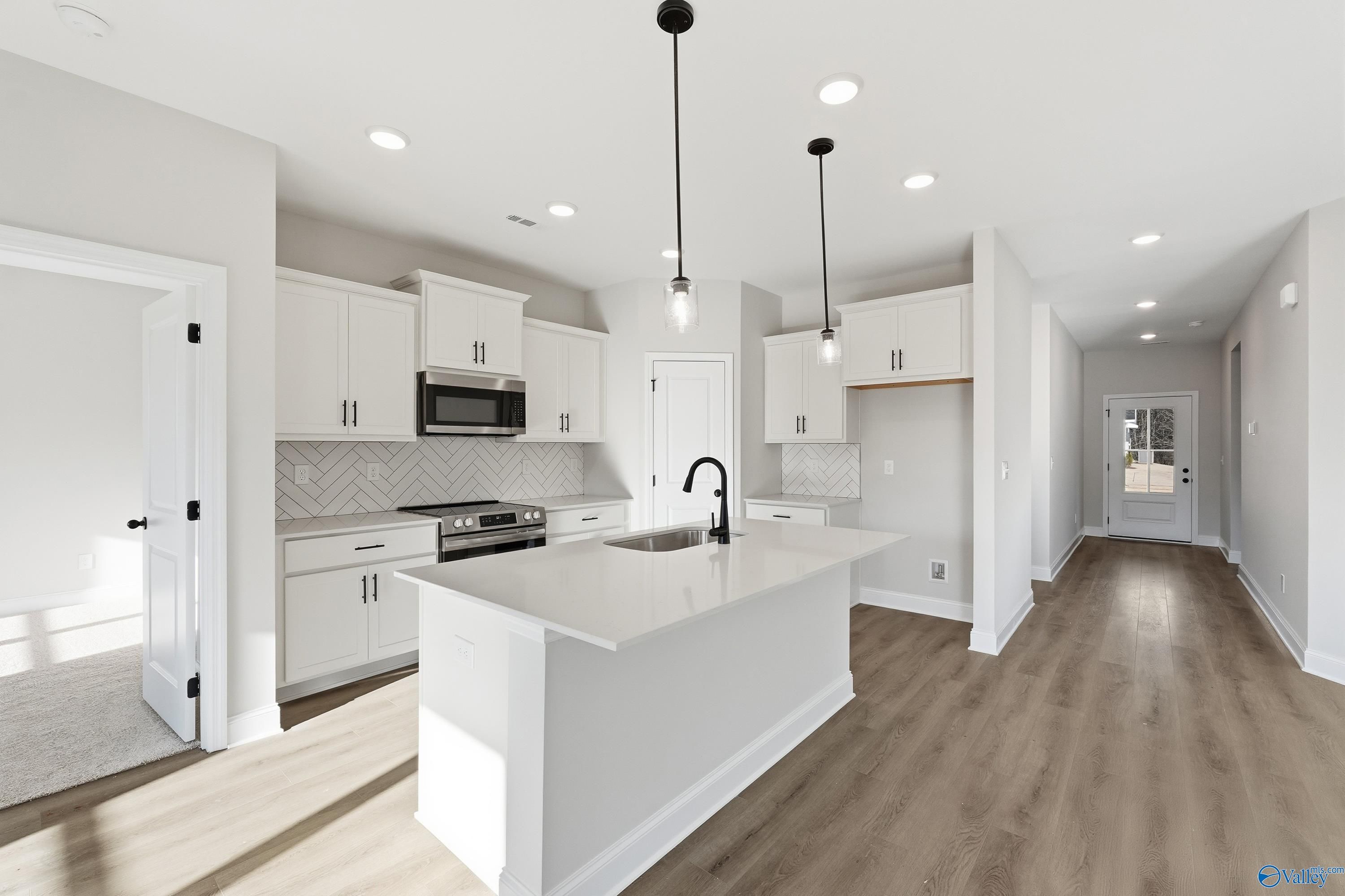 Modern open-concept kitchen with white cabinets, quartz island, stainless appliances, subway tile in Davidson Homes The Franklin E, Hazel Green, AL
