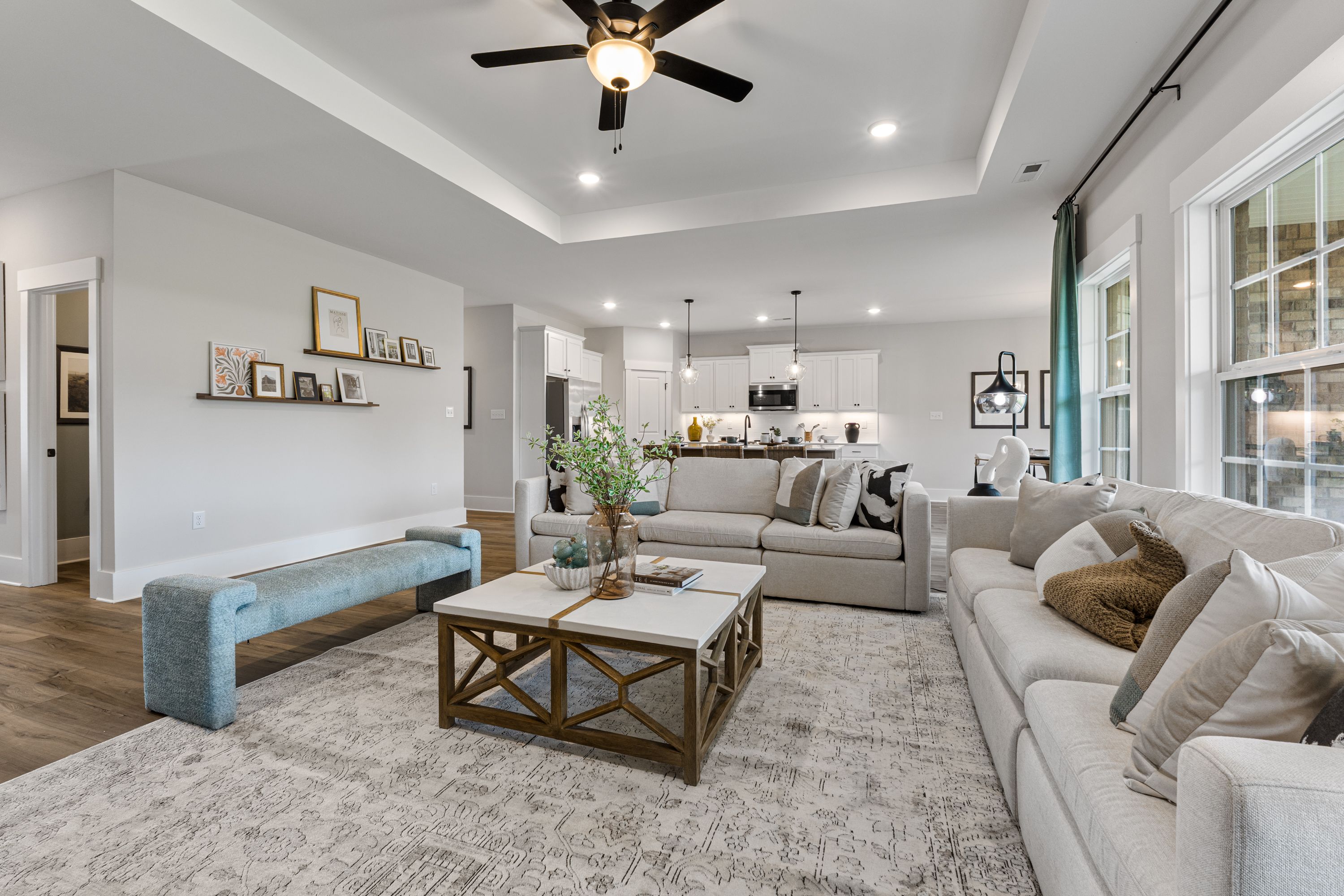 Open-concept living room at River Road Estates in Decatur Alabama featuring beige sofa, hardwood floors, large windows, and kitchen view