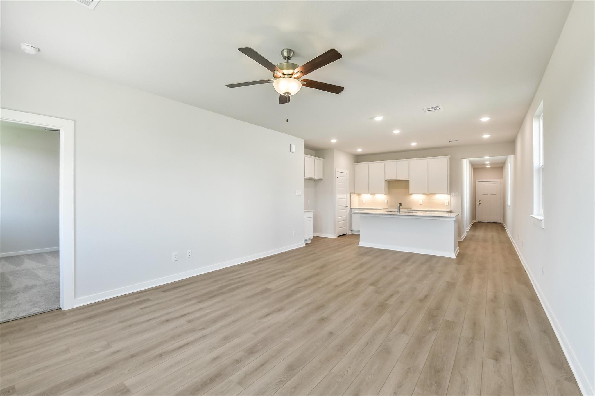 Open-concept living room and kitchen with white cabinets, island, and laminate wood floors in Davidson Homes The Colorado F, Cleveland Texas