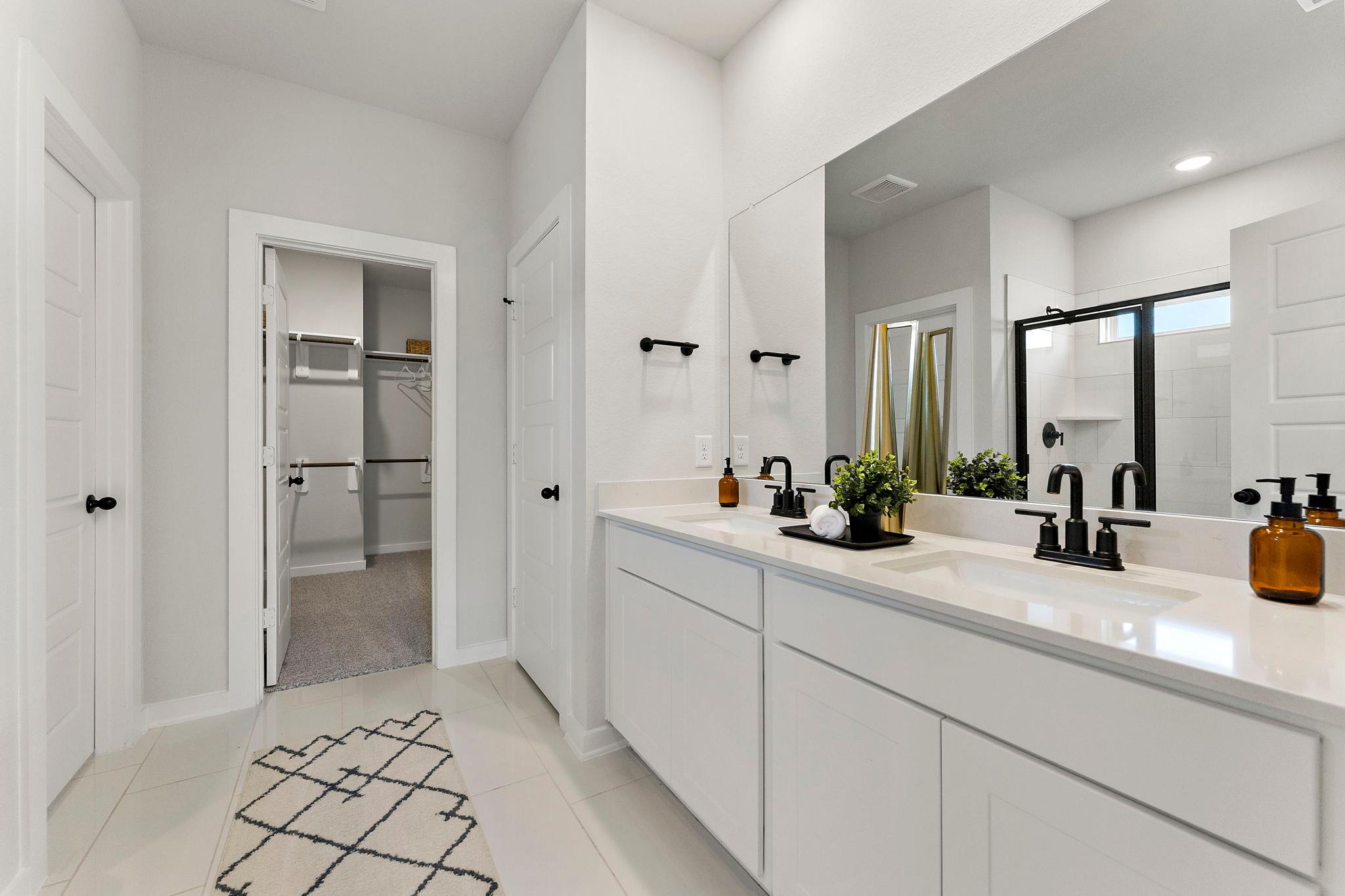 Spacious master bathroom at Sundance Cove in Crosby, Texas with double white vanity, black faucets, framed mirror, and walk-in shower