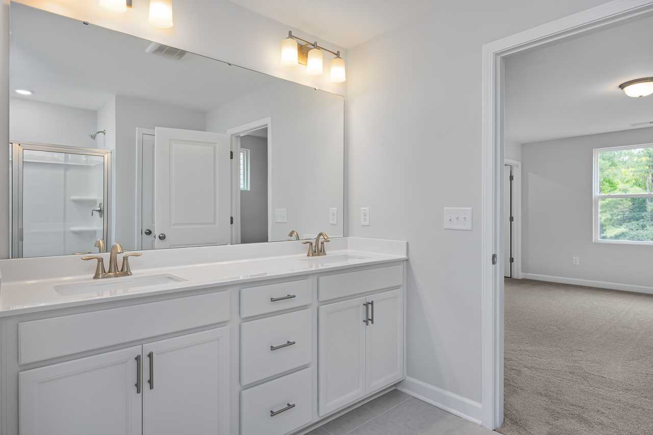 Modern master bathroom in The Durham D featuring double vanity, quartz counters, frameless shower, and soft lighting
