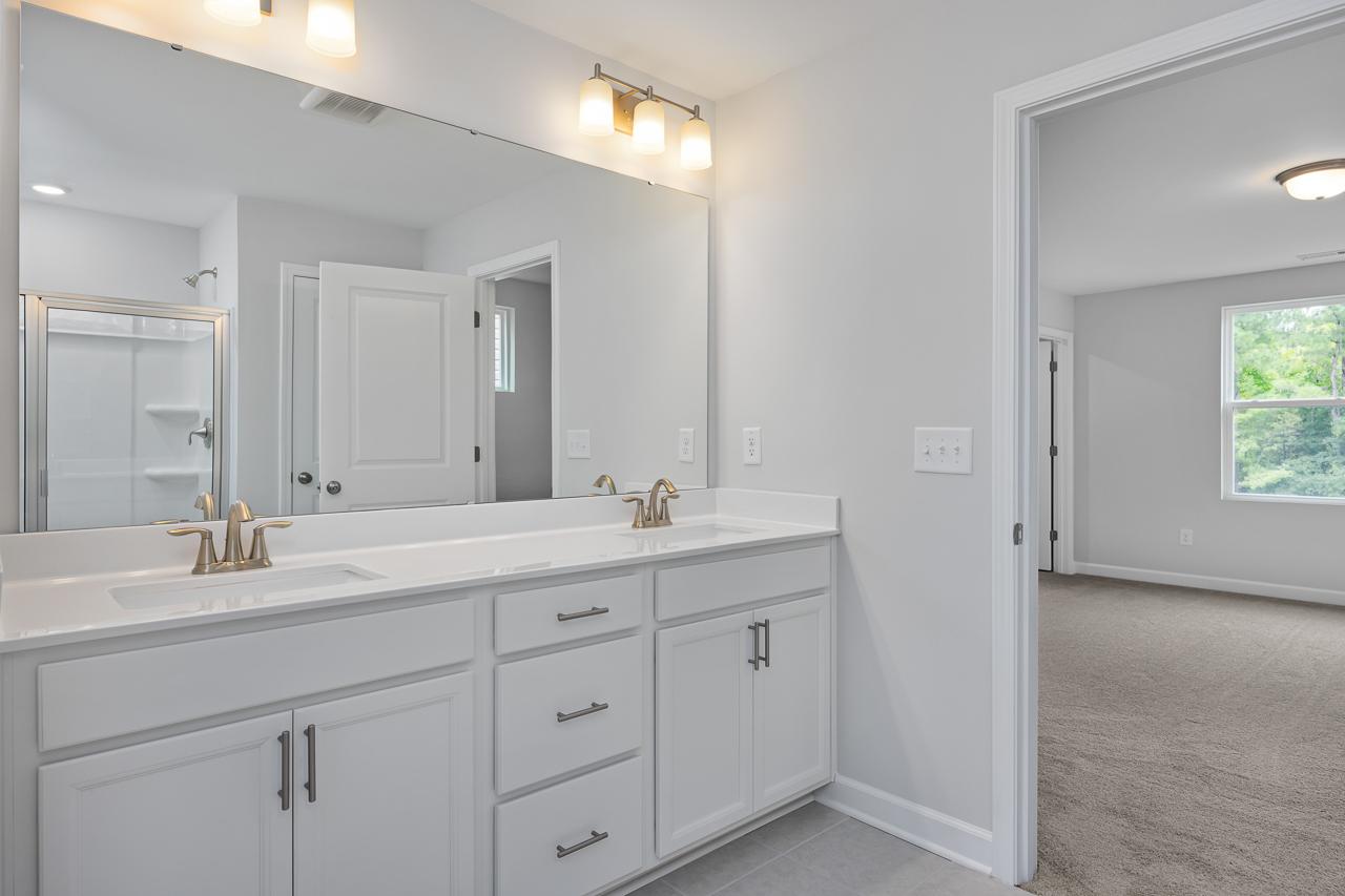 Spacious master bathroom in The Durham C featuring white double vanity, large mirror, and glass shower enclosure
