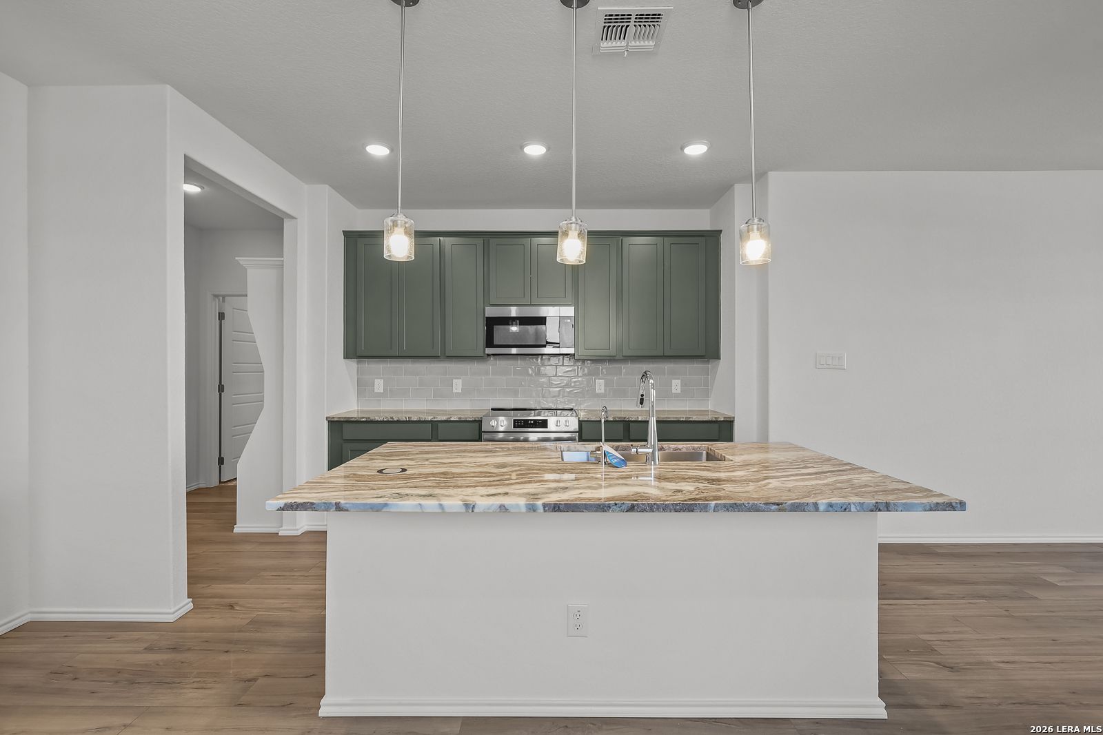 Modern kitchen with olive green cabinets, granite island, and pendant lighting in Brazos B floor plan, Agave, San Antonio.