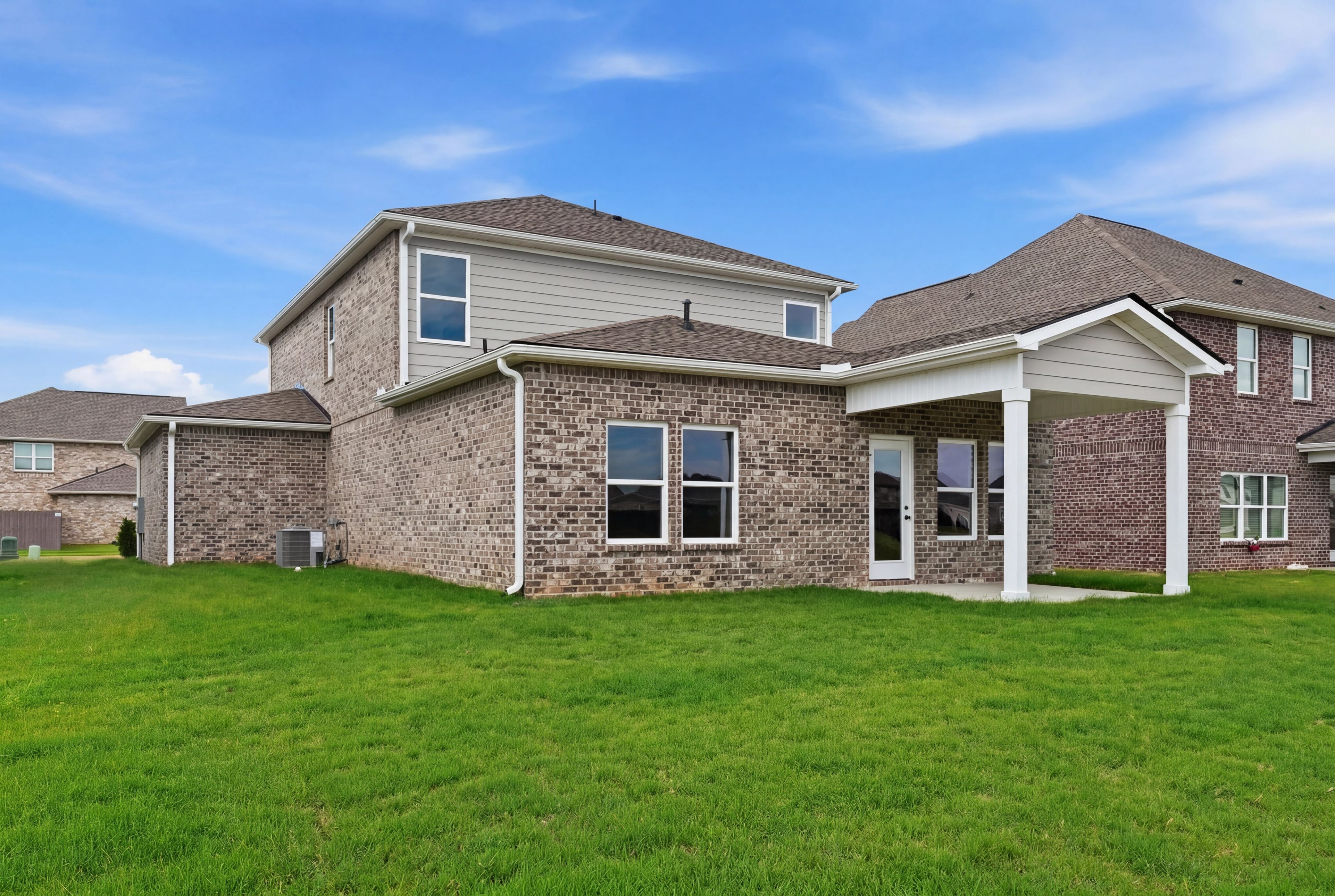 Rear view of The Meadowbrook home design featuring a brick exterior, covered patio, and spacious backyard.