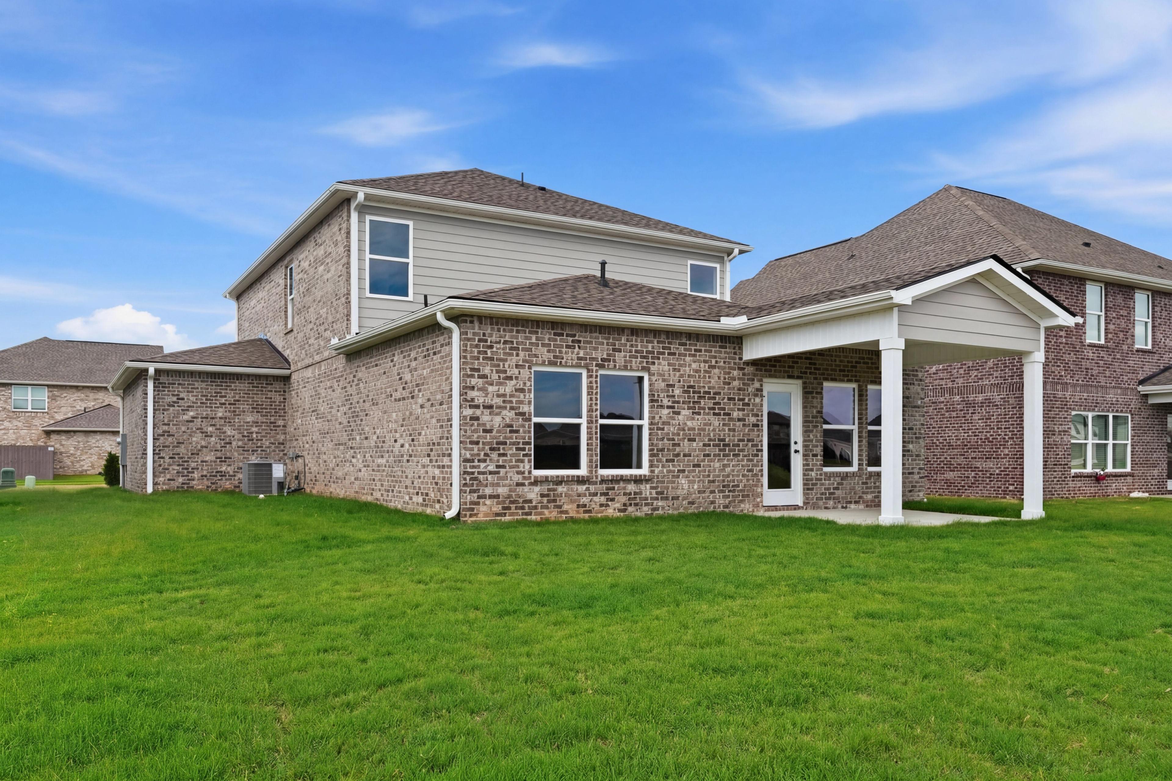 Rear view of The Meadowbrook home design featuring a brick exterior, covered patio, and spacious backyard.