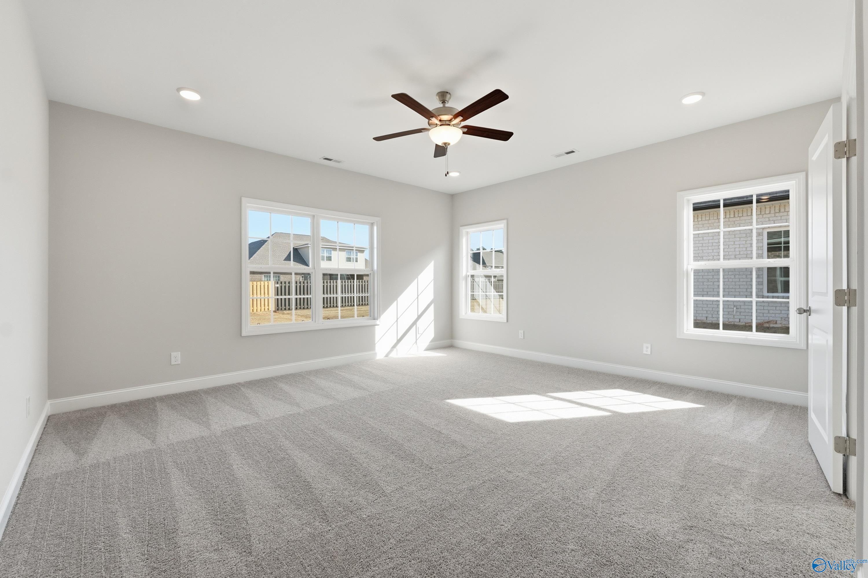 Spacious bedroom with gray carpet, ceiling fan, large windows, and natural light in Davidson Homes The Finleigh, Harvest, Alabama