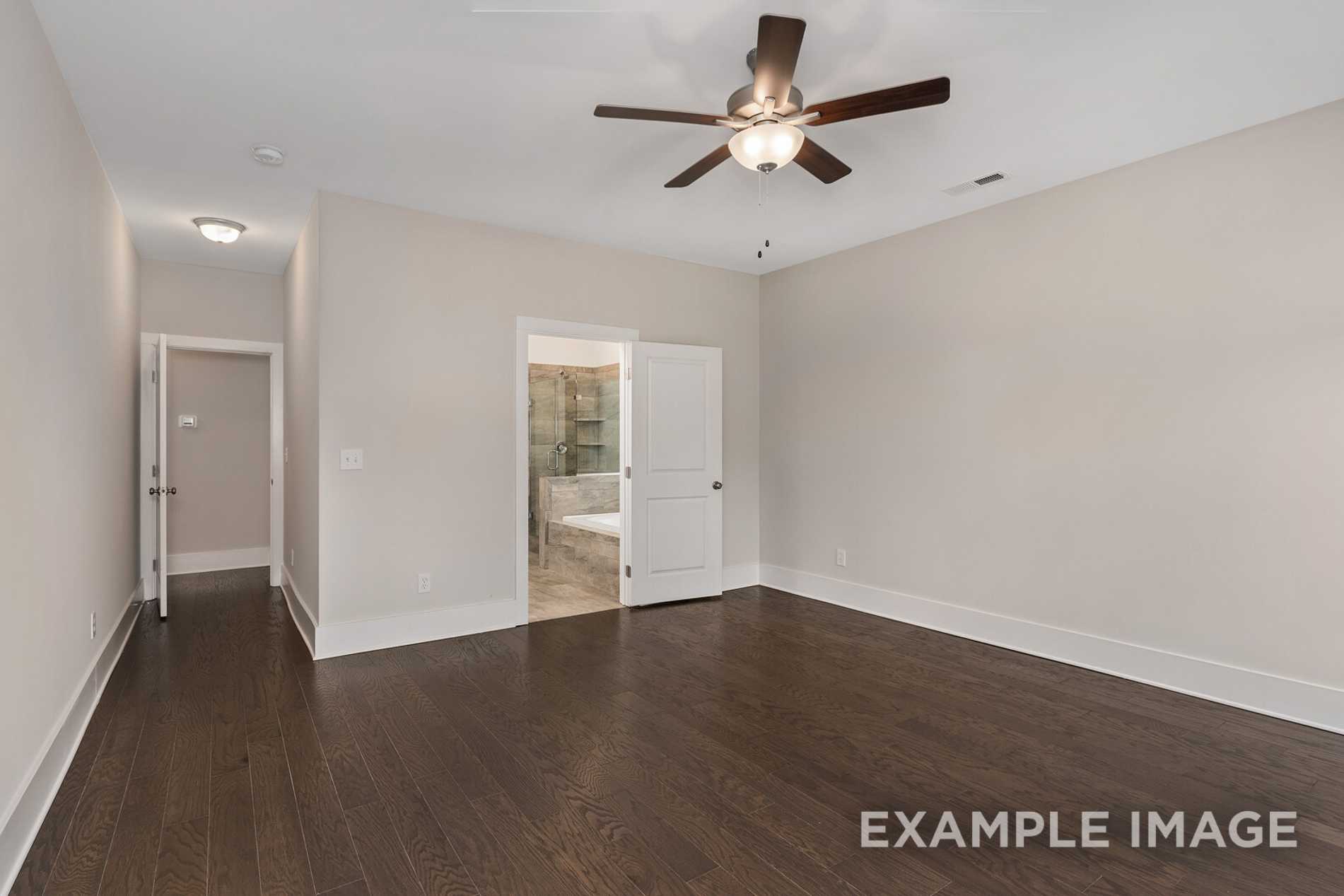 Spacious master bedroom in The Rockford plan with hardwood floors, ceiling fan, and en-suite bath access