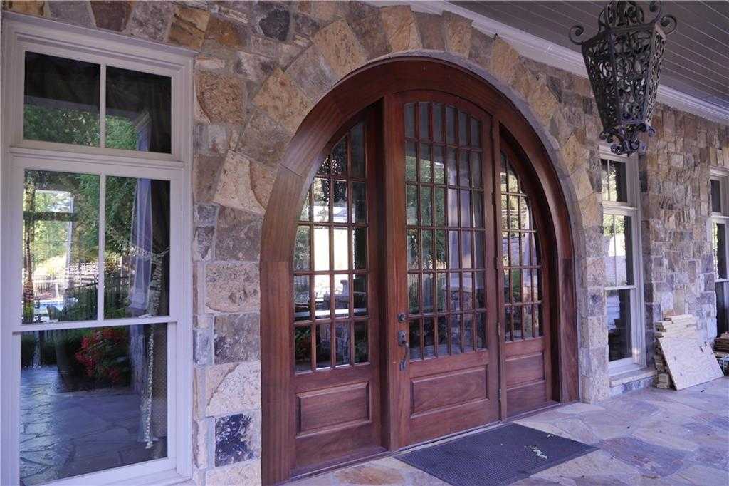 Grand arched mahogany double doors with stone facade and lantern on covered porch of Davidson Homes Seaside B in Woodstock, Georgia