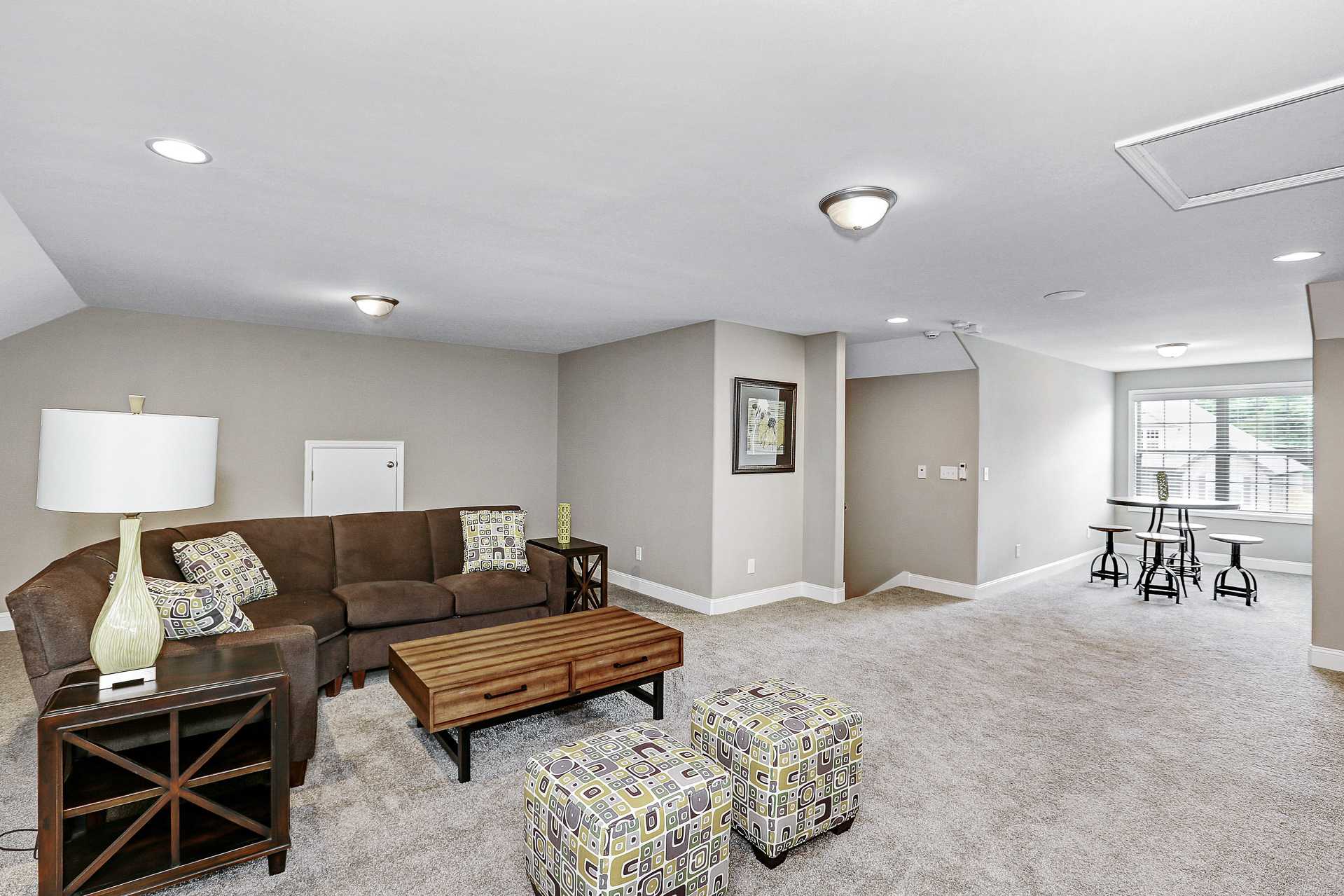 Bonus room with brown leather sectional sofa, wooden coffee table, and ottomans at Stone Creek Phase II in Cullman AL