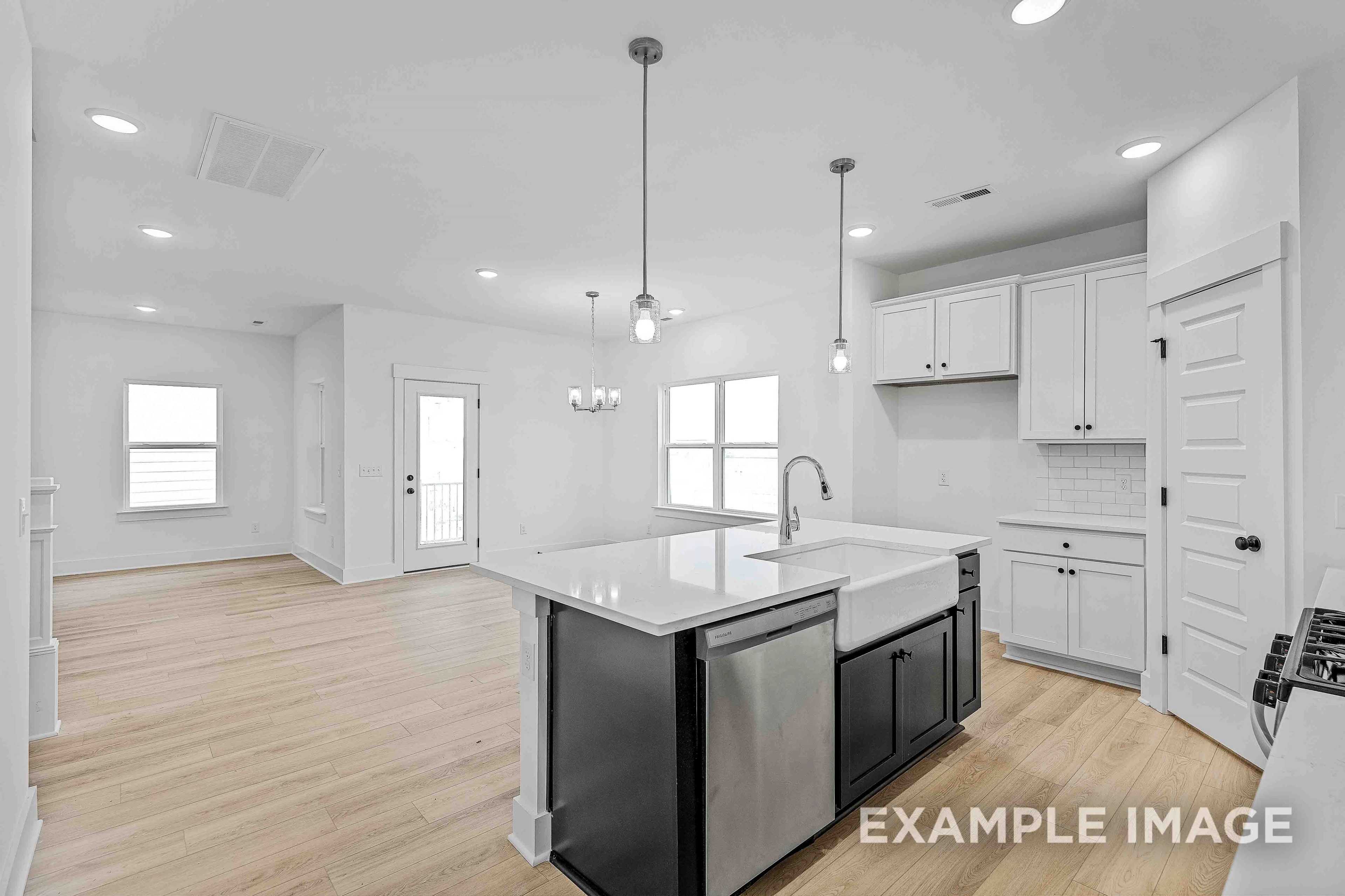 Spacious open kitchen in The Charleston home with white shaker cabinets, large quartz island, farmhouse sink, and hardwood floors