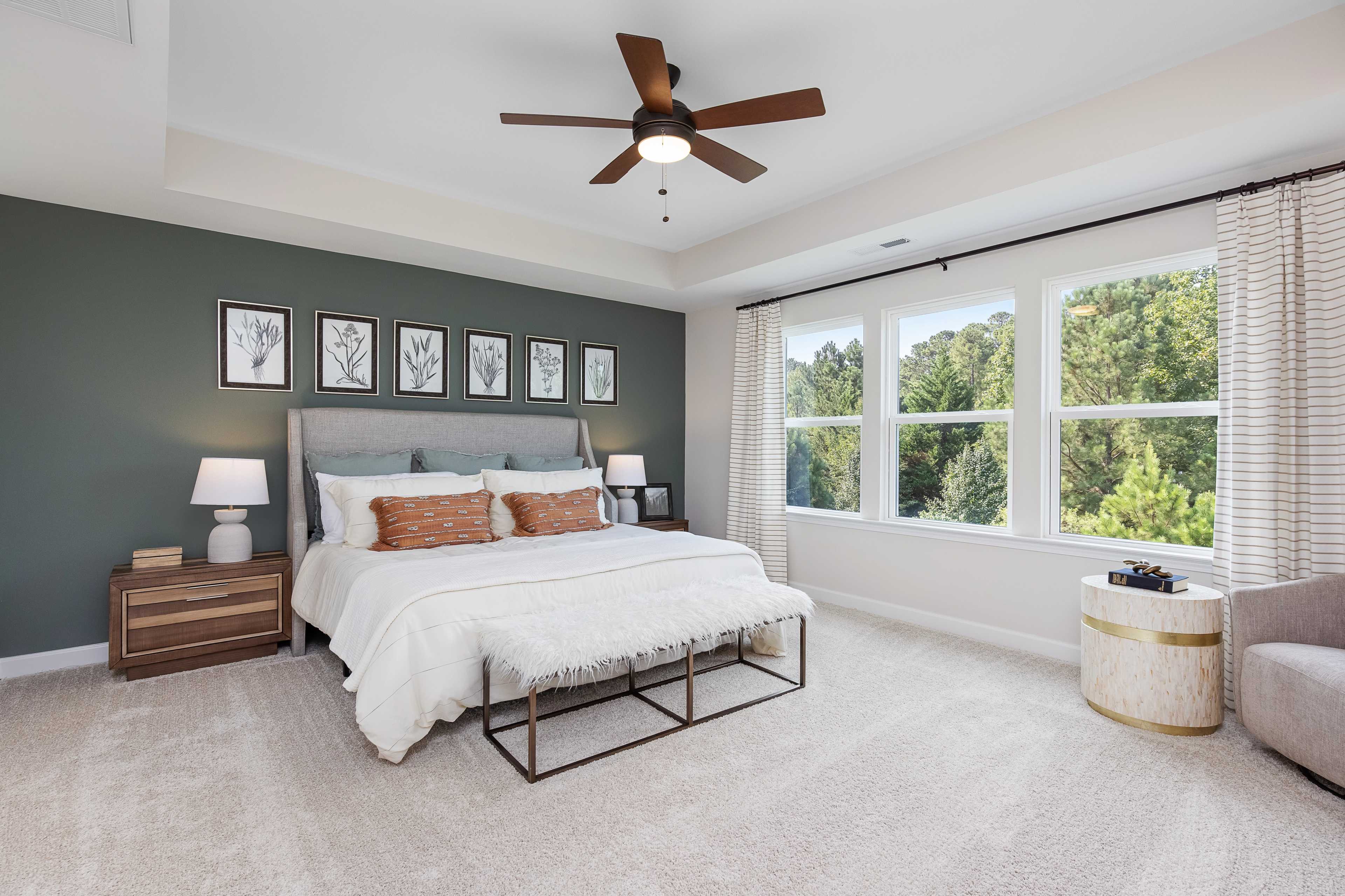 Spacious primary bedroom at Woodland Crossing in Zebulon NC with green accent wall, king bed, botanical art, and large wooded views