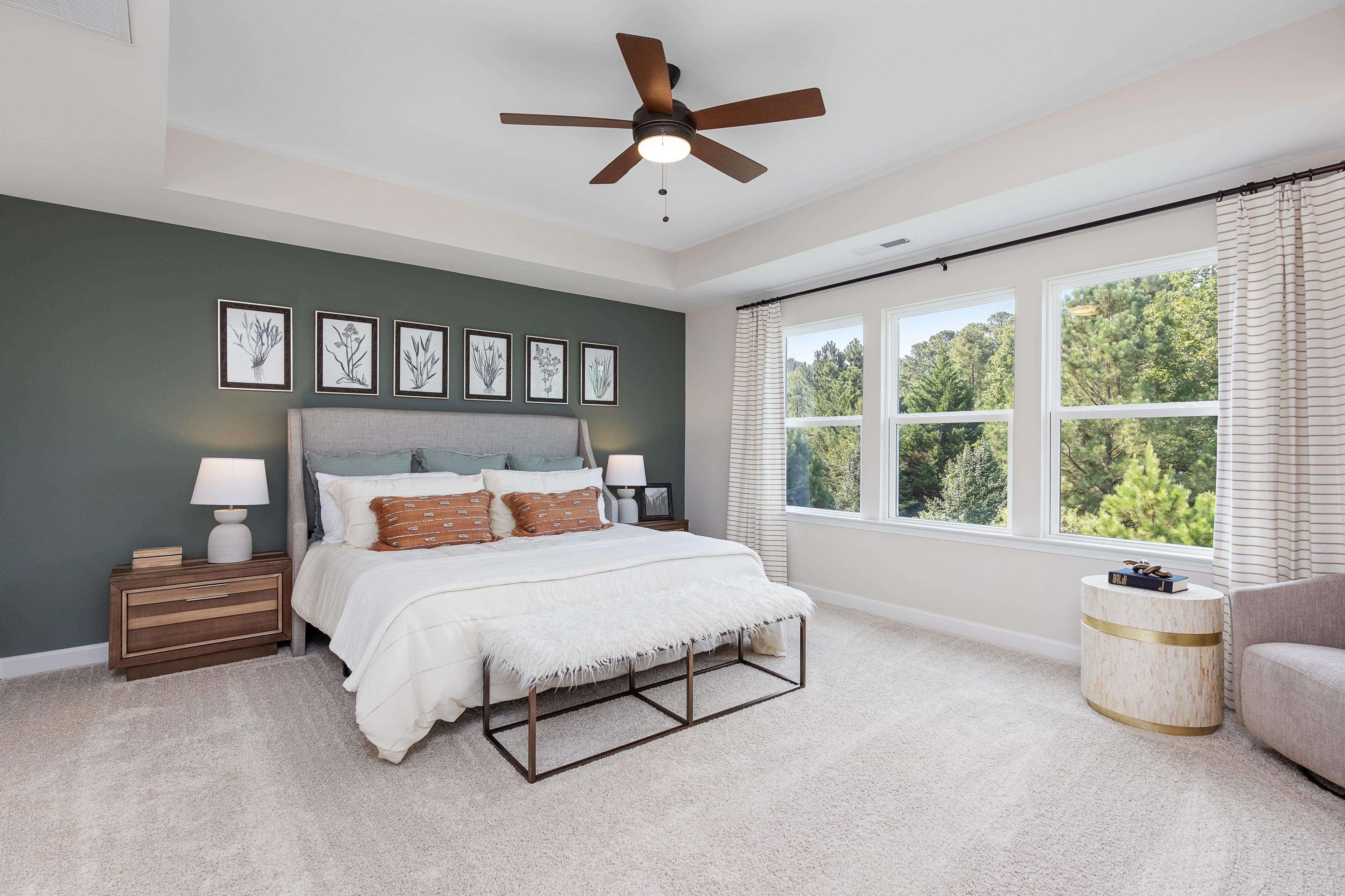 Spacious primary bedroom at Woodland Crossing in Zebulon NC with green accent wall, king bed, botanical art, and large wooded views