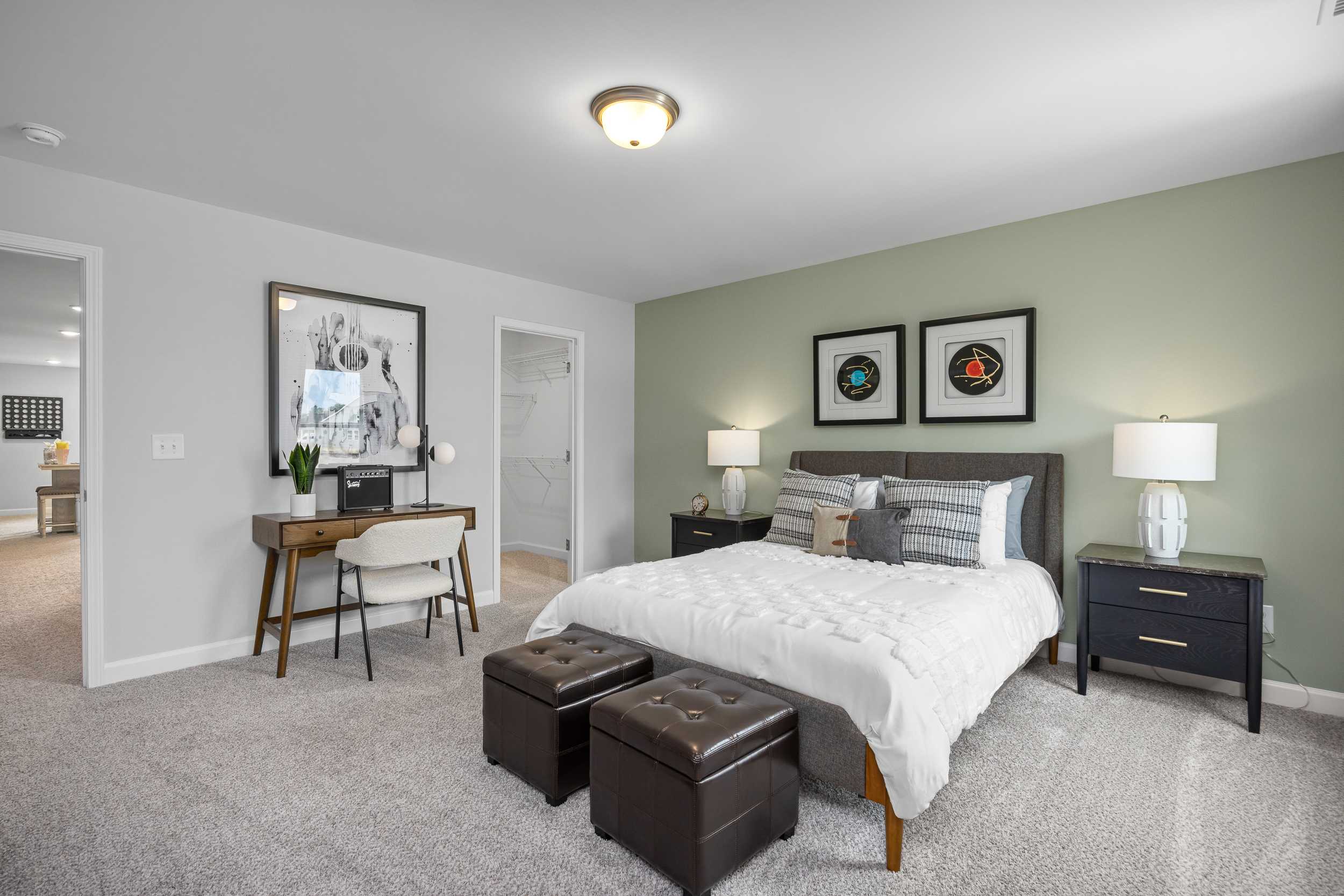Spacious master bedroom at Tobacco Road in Angier NC by Davidson Homes with green accent wall, king bed, desk, and modern lamps