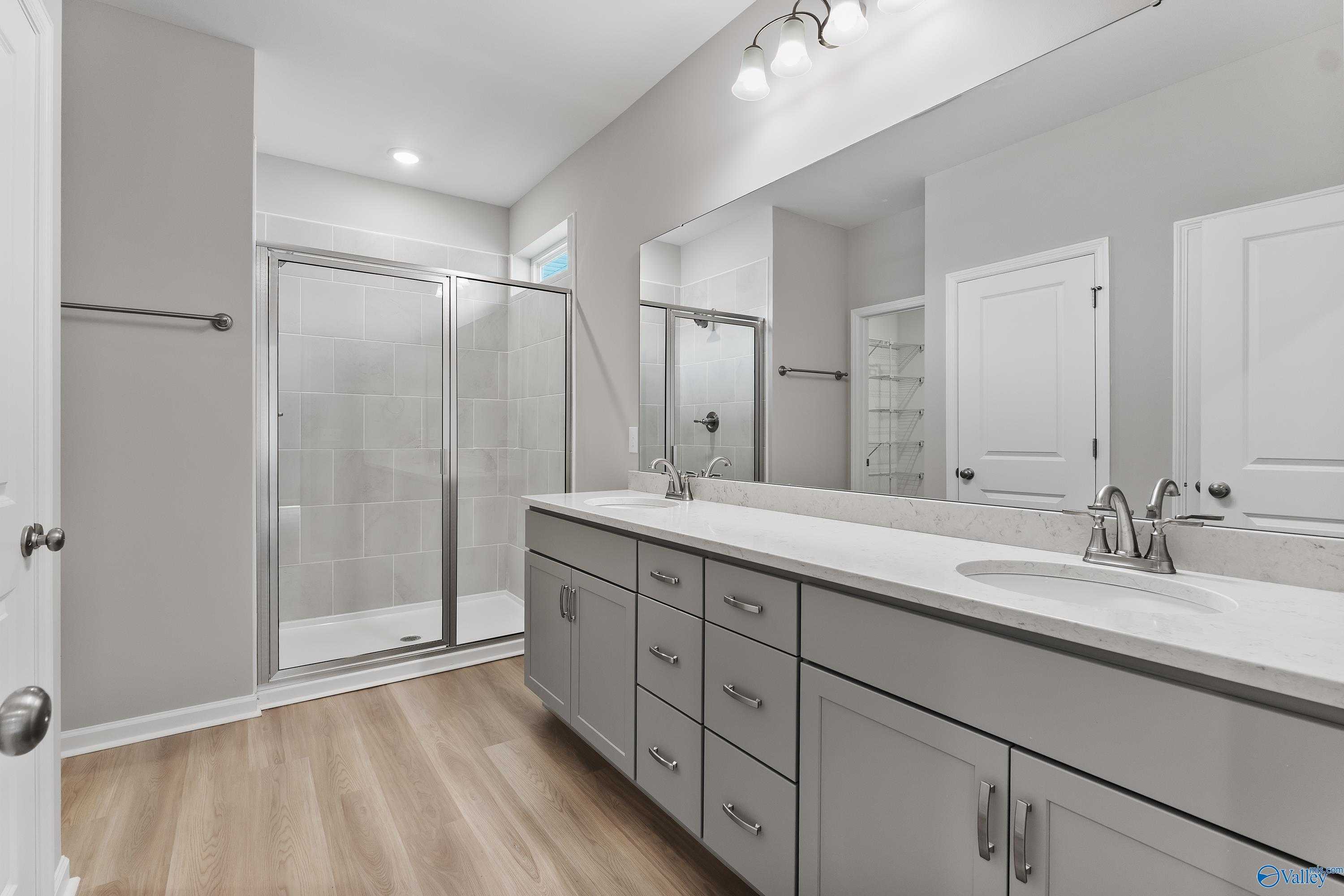 Modern master bathroom featuring glass shower, double vanity with quartz countertop, gray cabinets in The Grace by Evermore Homes, Madison AL
