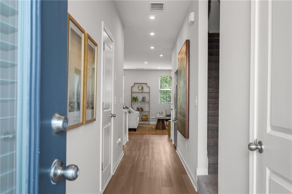 Inviting entry hallway with light wood floors, recessed lighting, and framed art leading to stairs and living room in Davidson Homes The Durant A, Emerson, Georgia