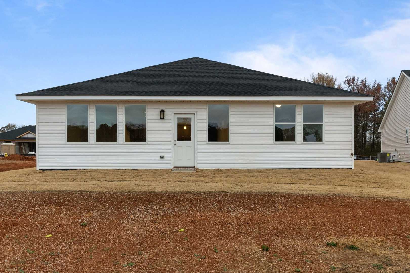 Rear view of The Luna 1-story home in Perry, GA, with white siding, black roof, large windows, and covered patio by Evermore Homes