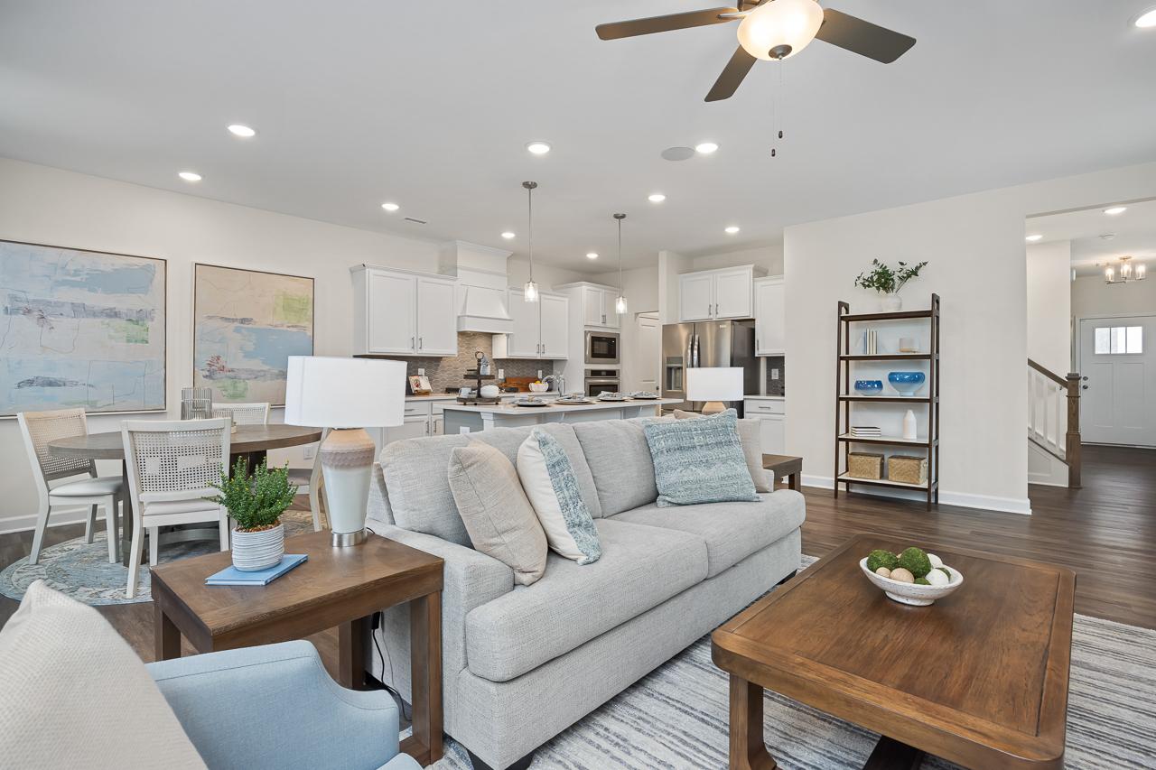 Spacious open-concept living room at Gregory Village Townhomes in Lillington NC with gray sofa, wooden tables, white kitchen cabinets, and ceiling fan