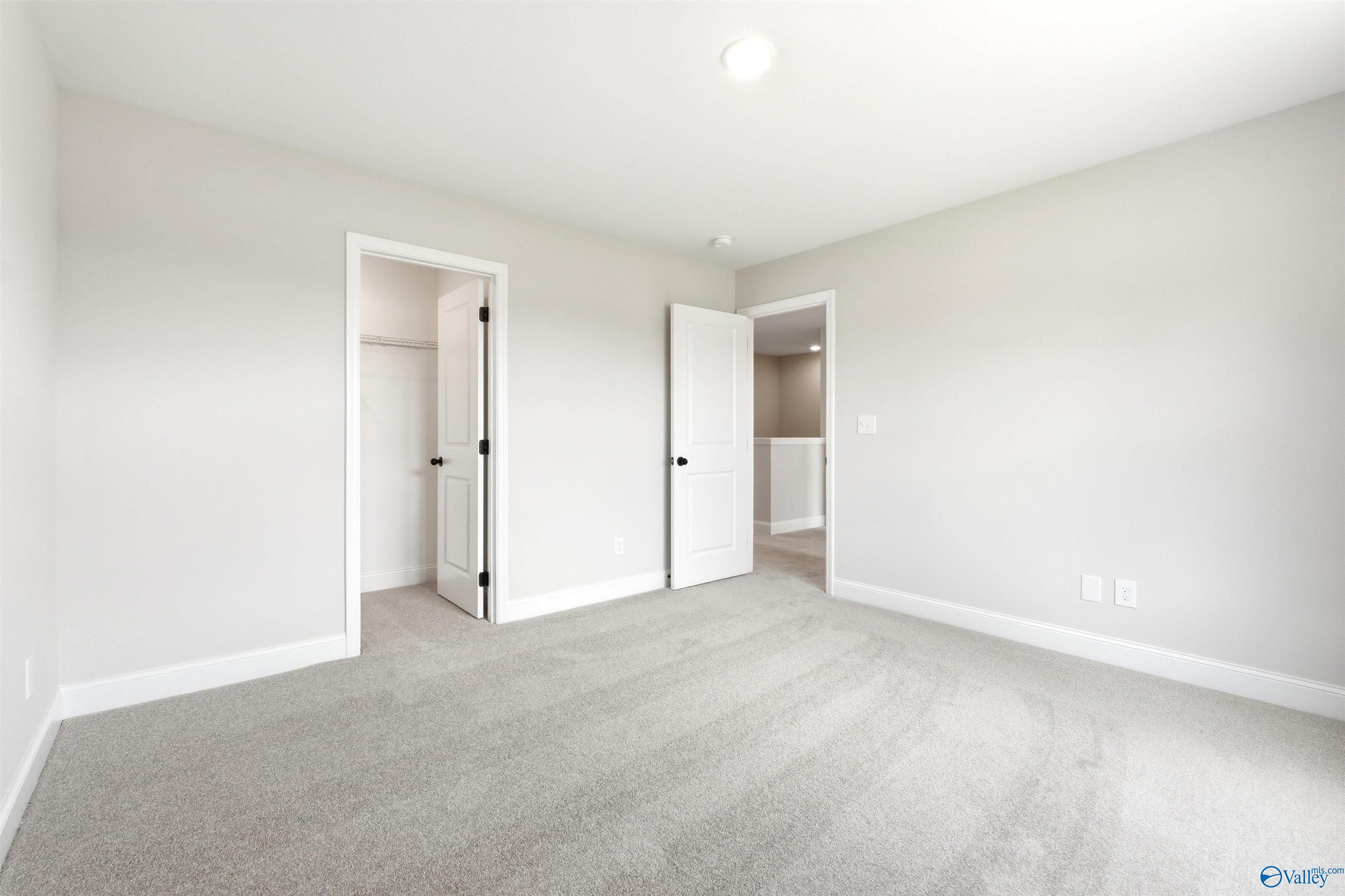 Spacious secondary bedroom with neutral carpet and walk-in closet in The Shelby A floor plan at Wood Trail, Toney, Alabama.