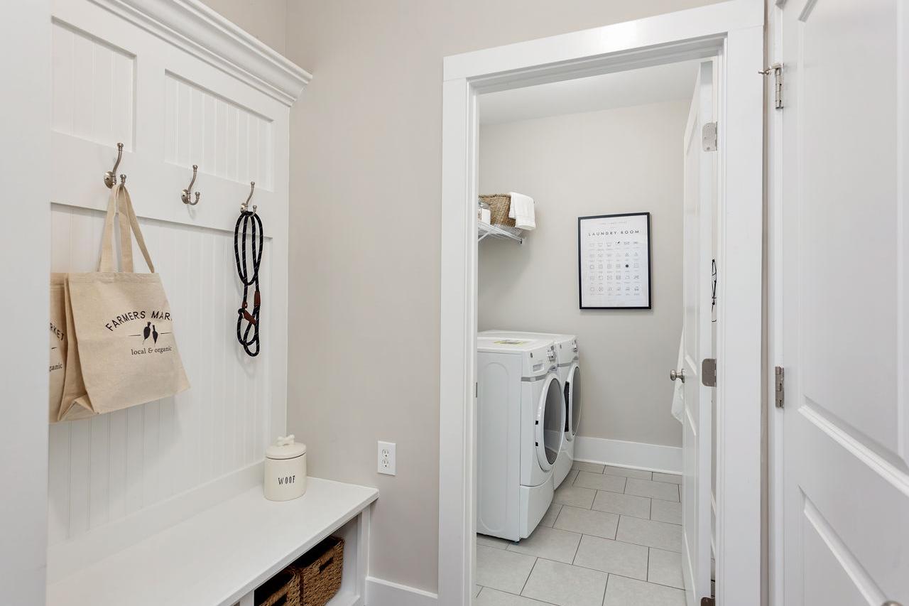 Spacious mudroom at Laurenwood Preserve in Madison AL with white beadboard cabinets, hooks, bench, baskets and adjacent laundry room