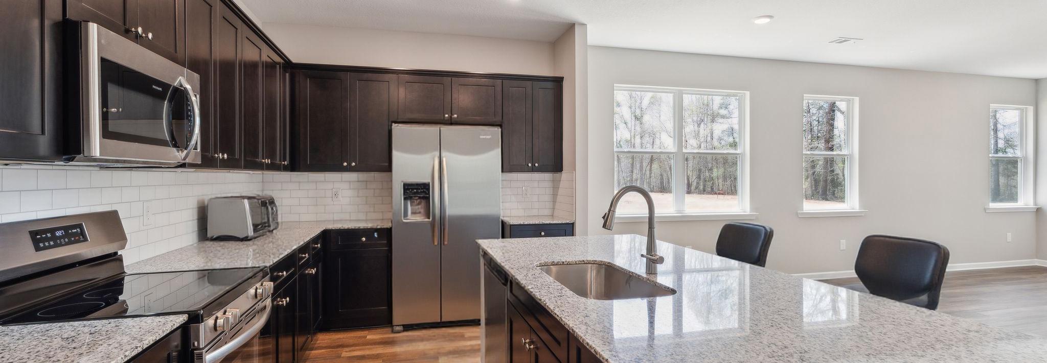 Modern kitchen in Heatherbrook Phenix City Alabama with dark cabinets granite island stainless appliances and hardwood floors