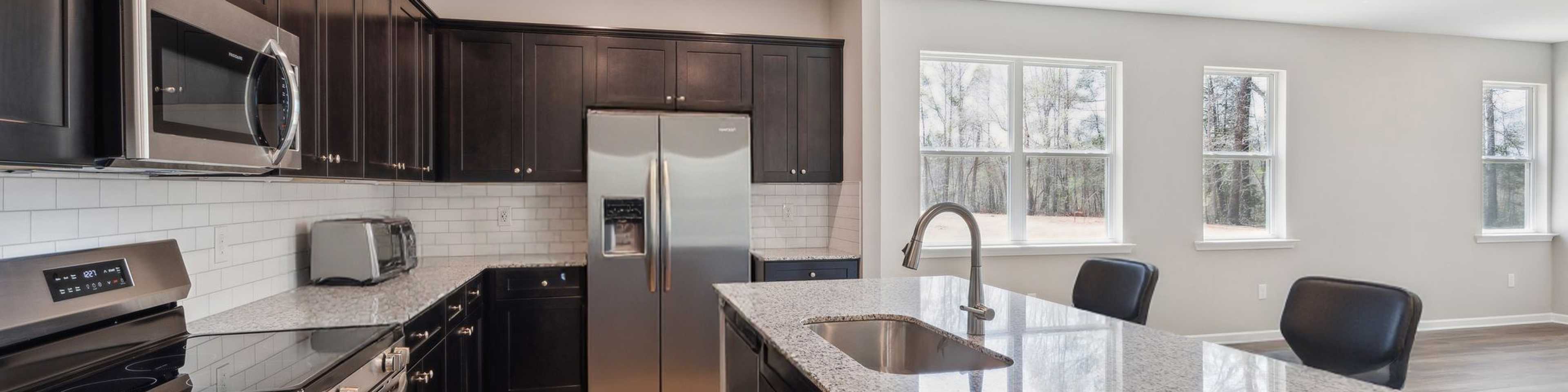 Modern kitchen in Heatherbrook Phenix City Alabama with dark cabinets granite island stainless appliances and hardwood floors