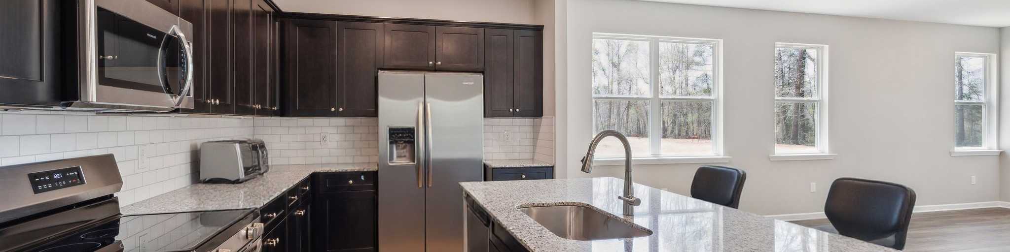 Modern kitchen in Heatherbrook Phenix City Alabama with dark cabinets granite island stainless appliances and hardwood floors