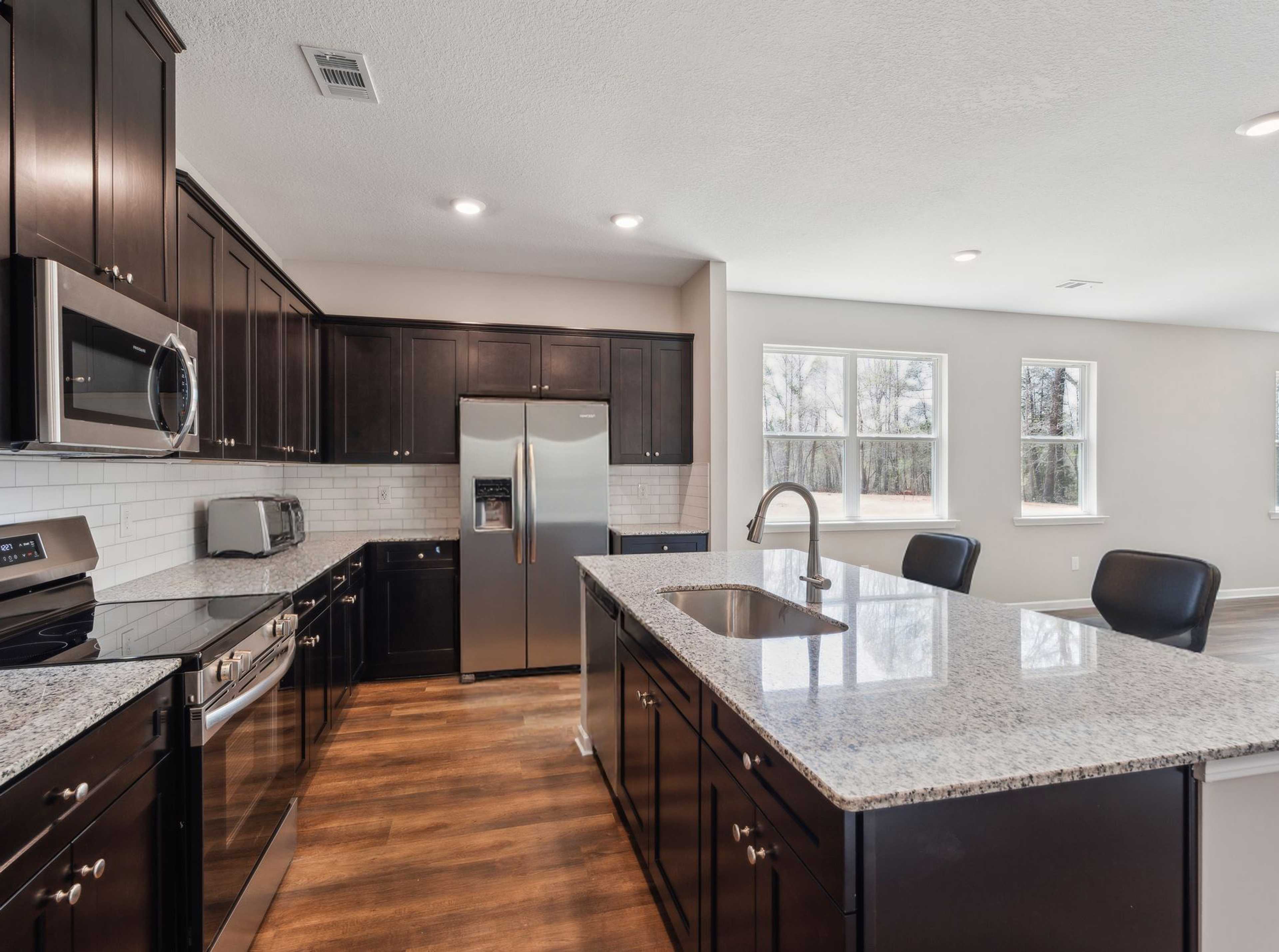 Modern kitchen in Heatherbrook Phenix City Alabama with dark cabinets granite island stainless appliances and hardwood floors