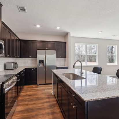 Modern kitchen in Heatherbrook Phenix City Alabama with dark cabinets granite island stainless appliances and hardwood floors