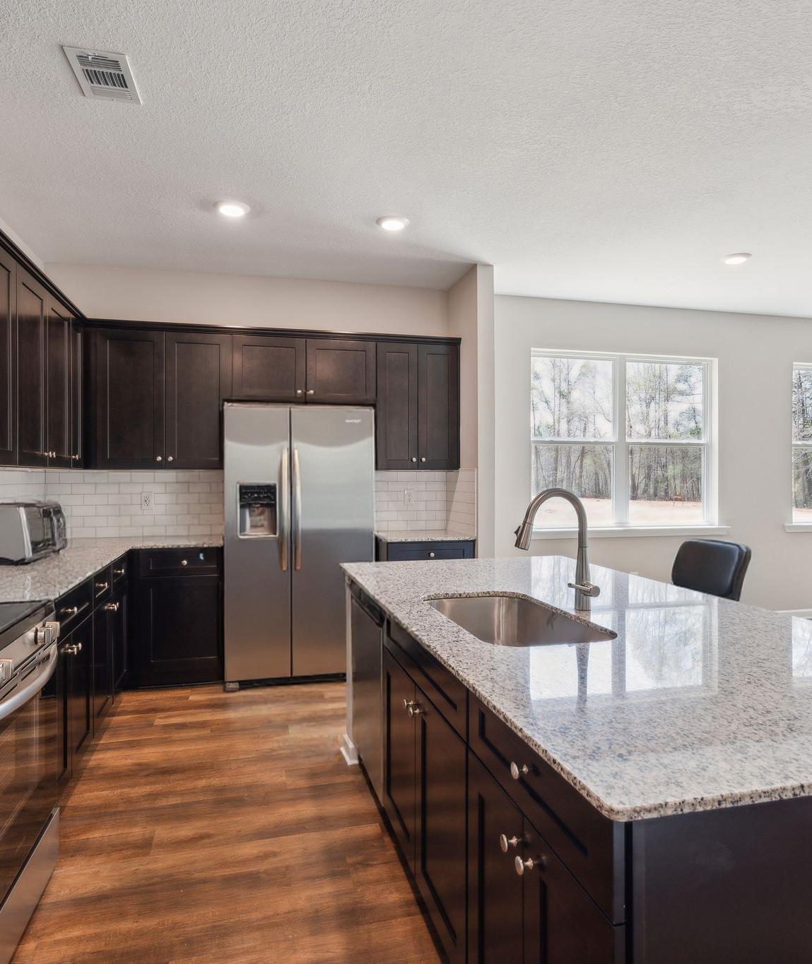 Modern kitchen in Heatherbrook Phenix City Alabama with dark cabinets granite island stainless appliances and hardwood floors