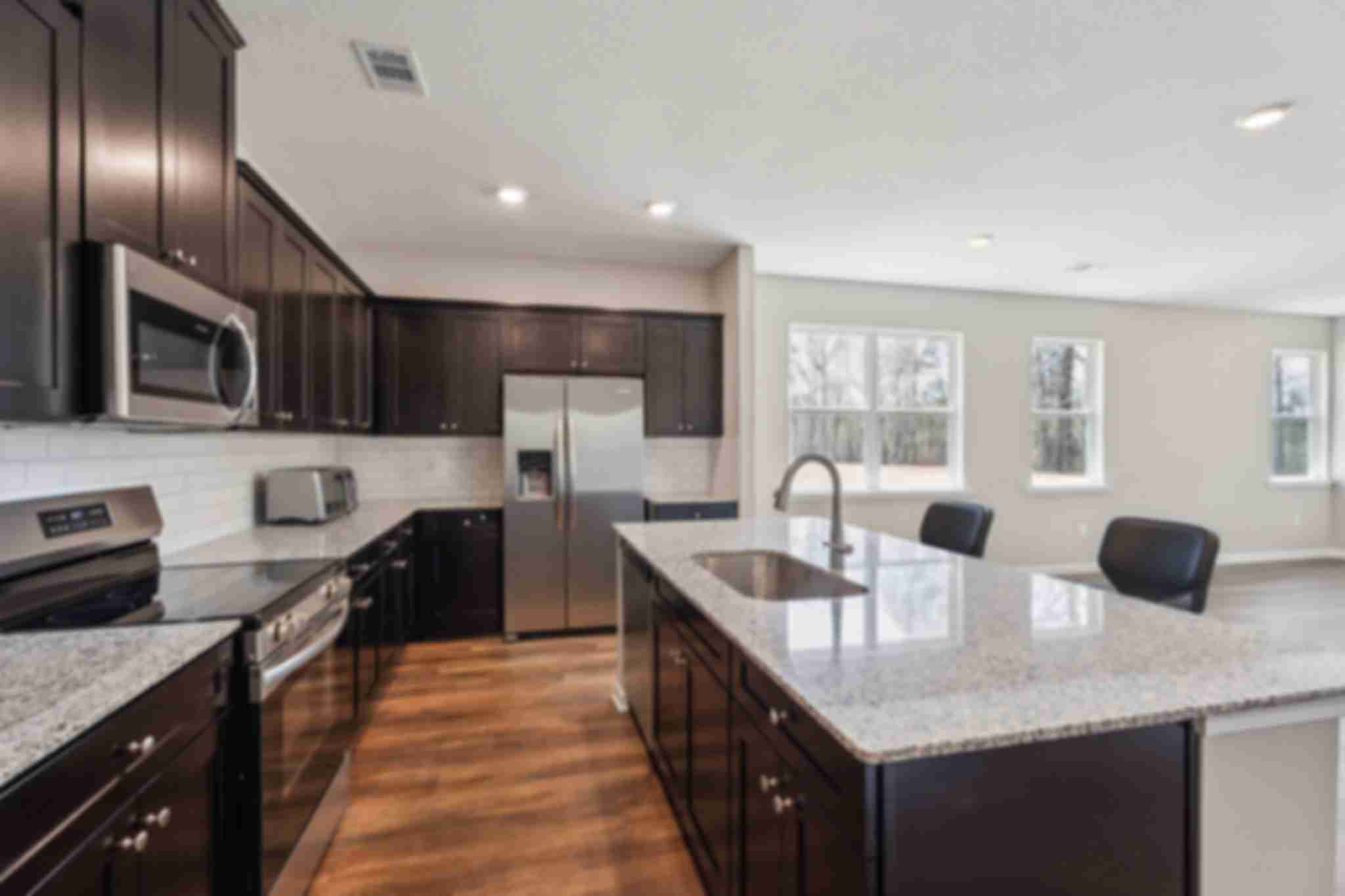 Modern kitchen in Heatherbrook Phenix City Alabama with dark cabinets granite island stainless appliances and hardwood floors