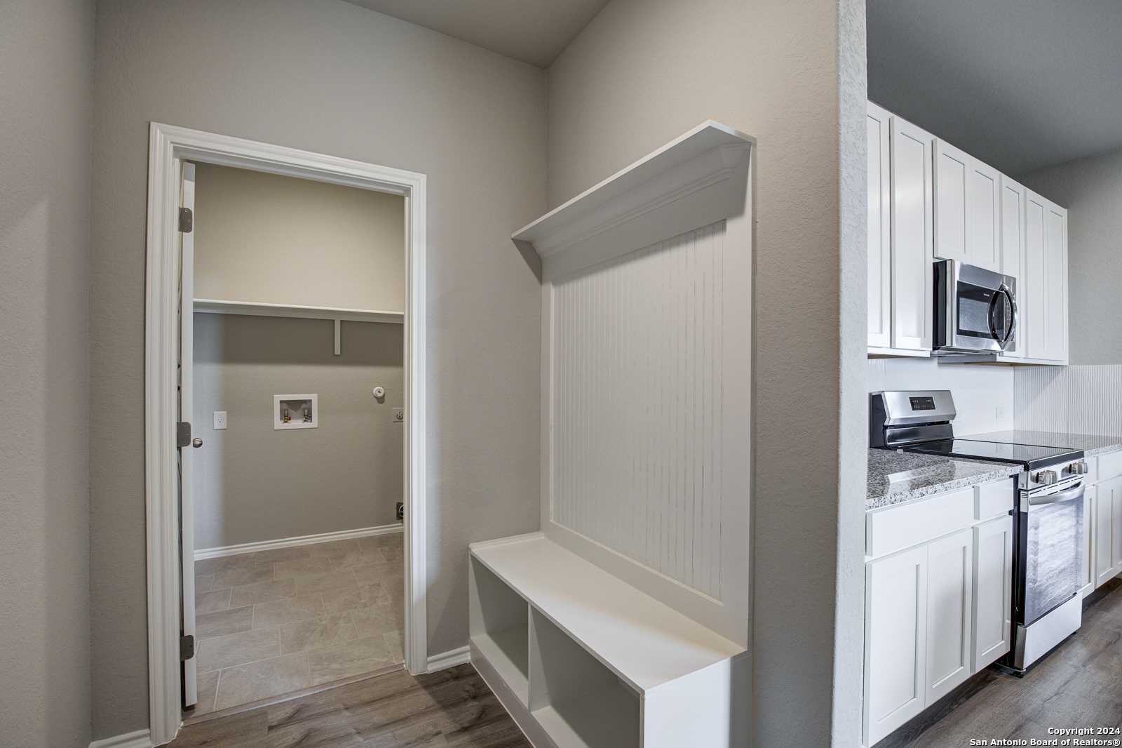 Modern laundry room with washer-dryer and open mudroom bench, adjacent white kitchen in Davidson Homes The Blanco C, San Antonio